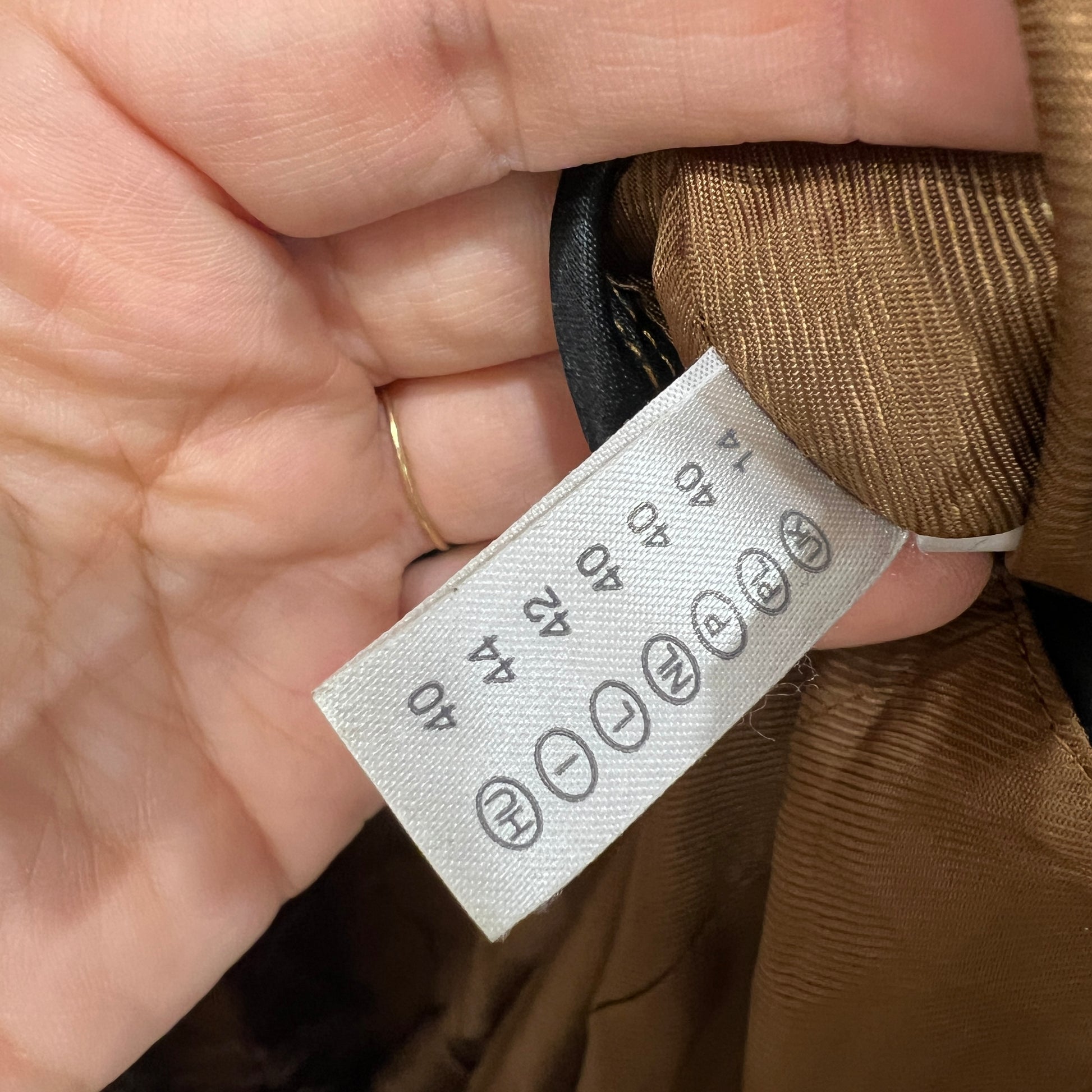 Close-up of a clothing tag on a brown fabric with a hand holding it