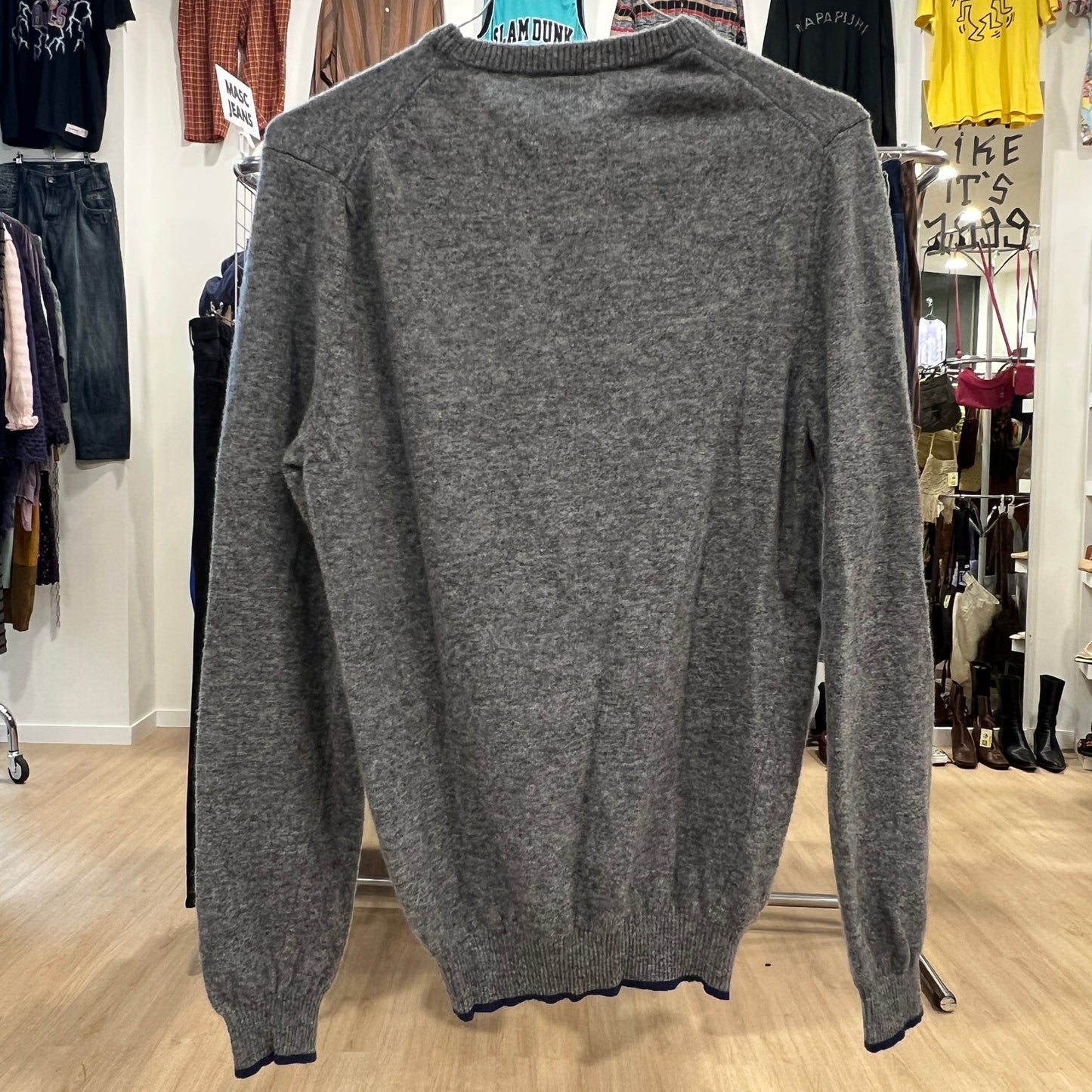 Gray sweater on a hanger in a store setting with various clothing items in the background