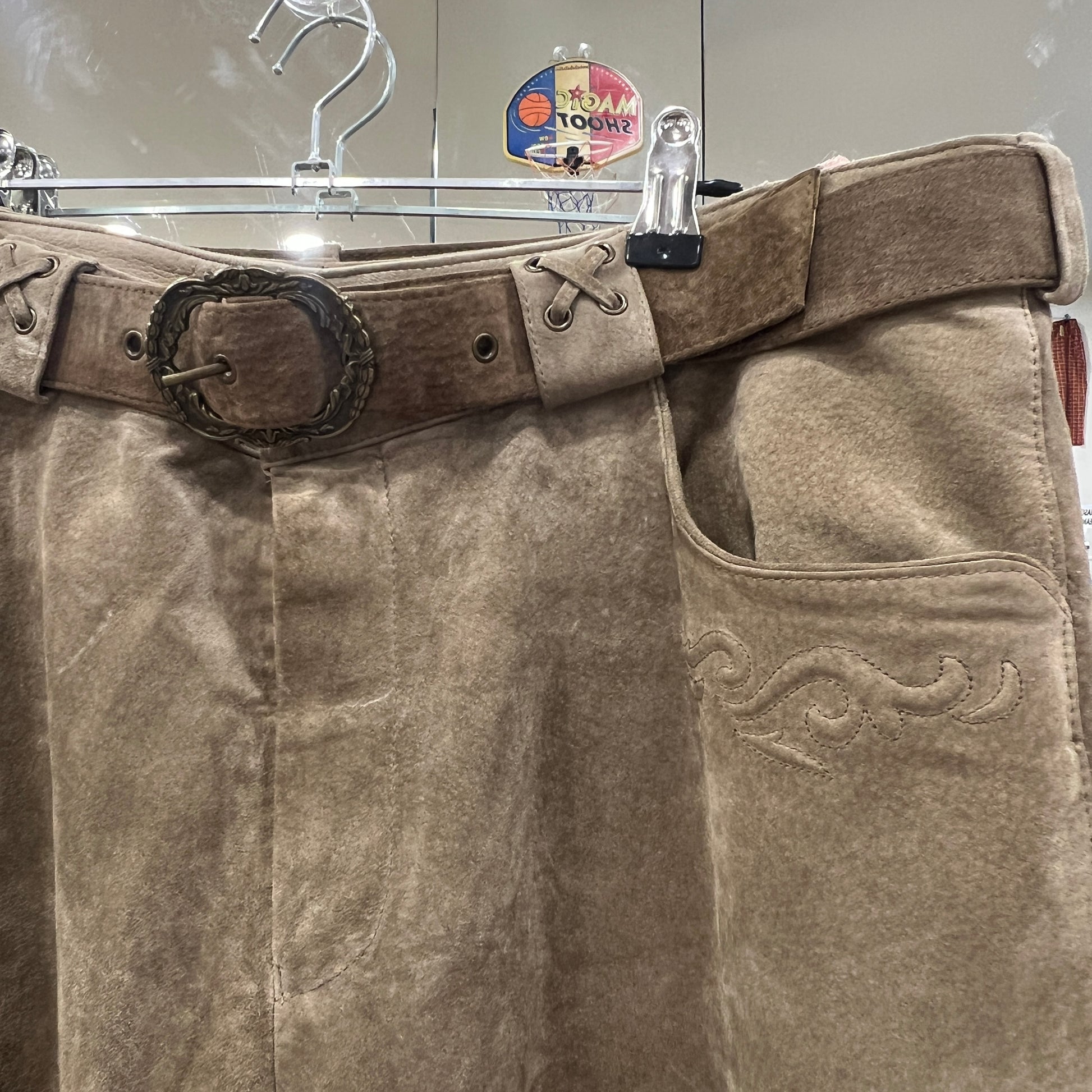 Brown leather pants with a belt and decorative buckle on a hanger