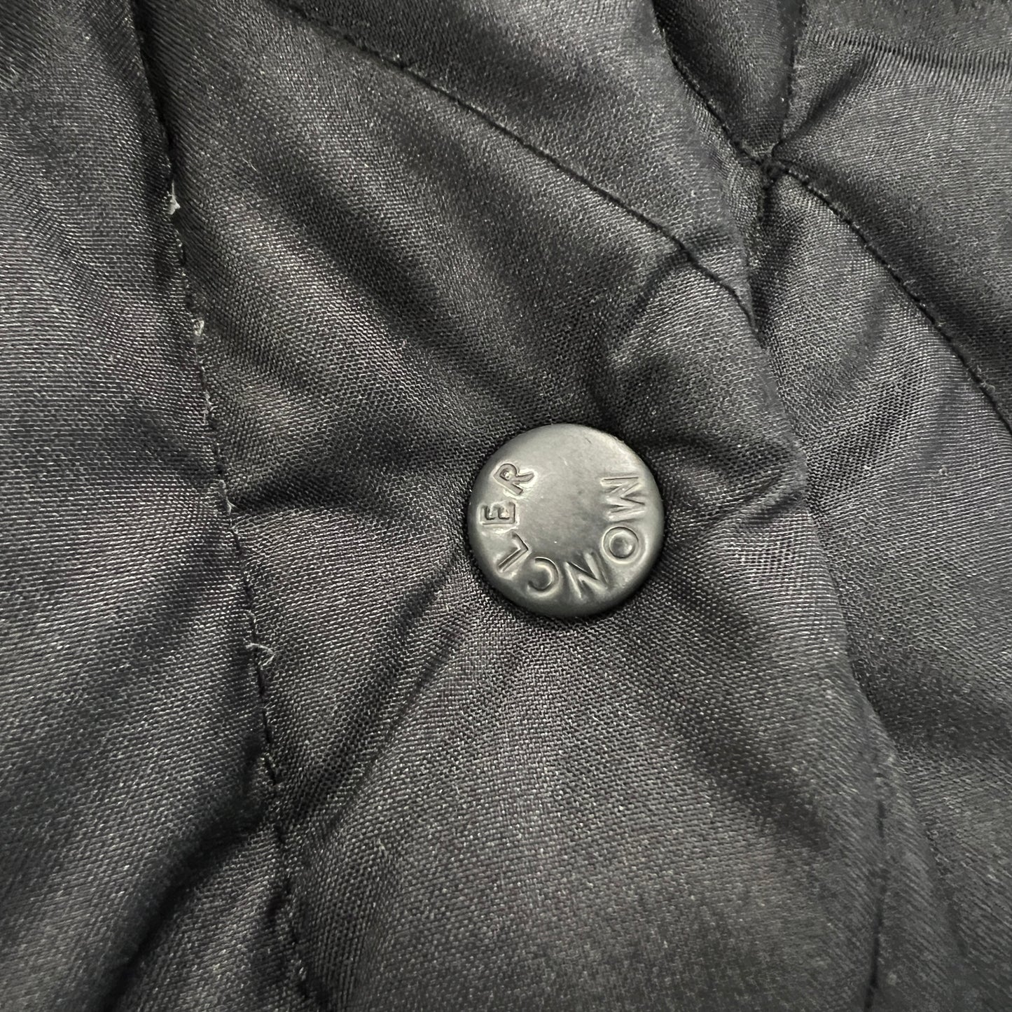 Close-up of a button on a textured fabric surface with 'Moncler' branding