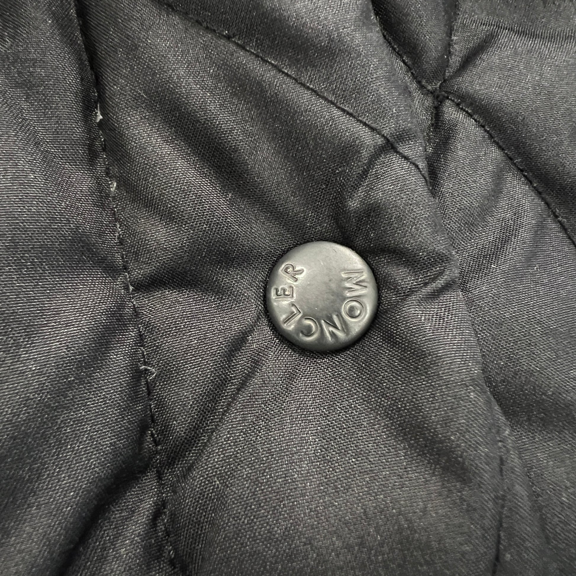 Close-up of a button on a textured fabric surface with 'Moncler' branding
