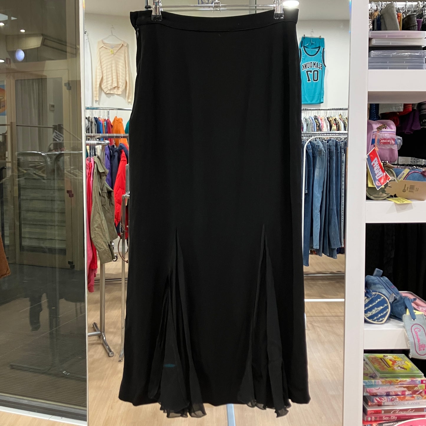 Black dress on a hanger in a store setting with clothing racks and shelves in the background