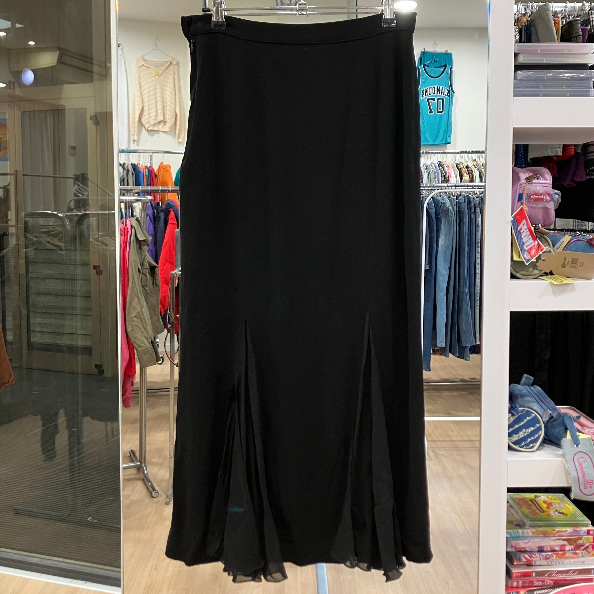 Black dress on a hanger in a store setting with clothing racks and shelves in the background