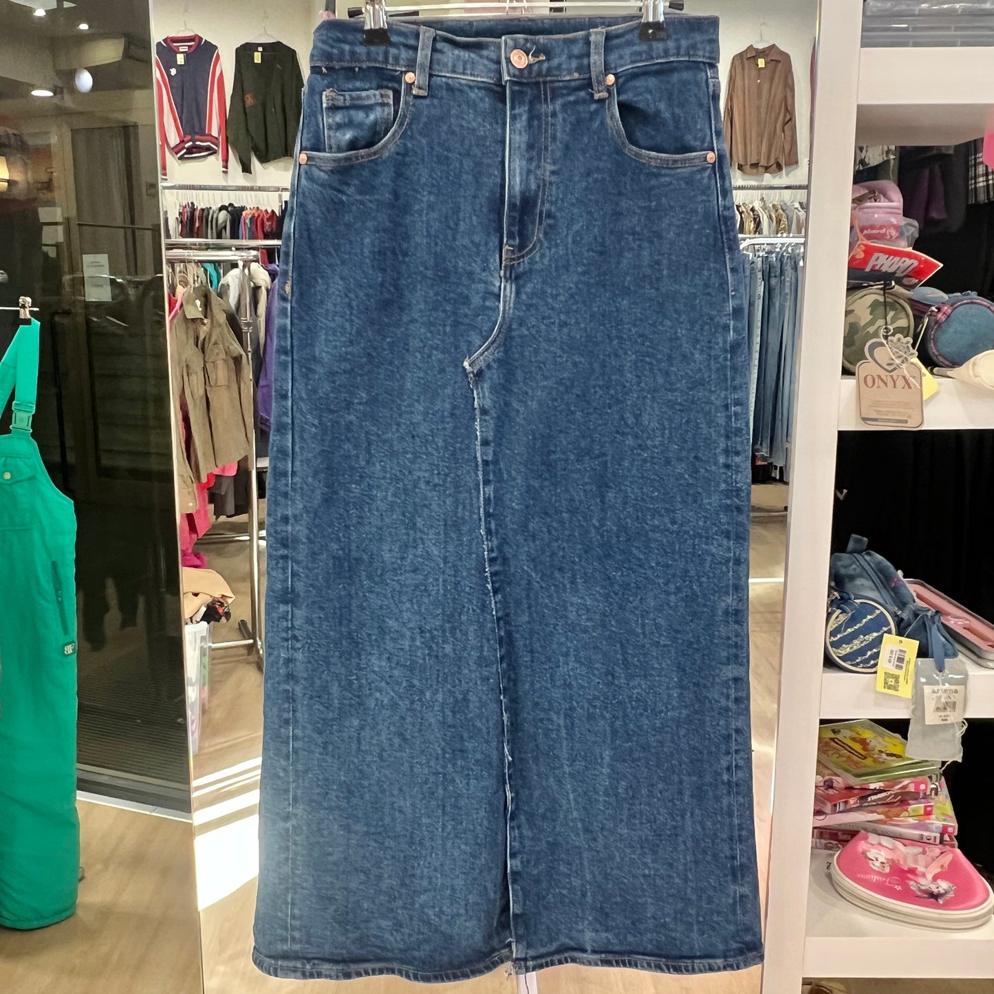 Blue denim skirt on a hanger in a store setting with various clothing items in the background