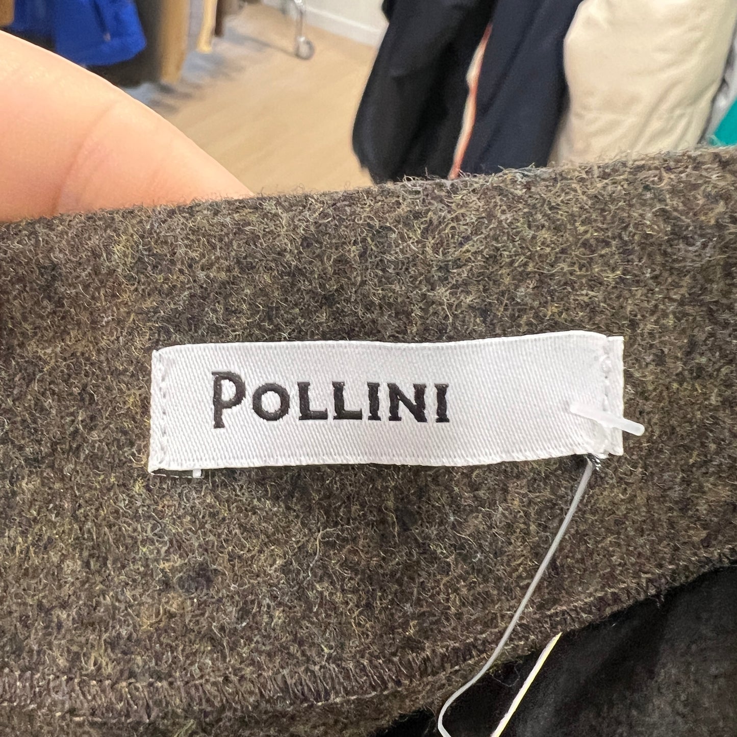 Close-up of a white Pollini brand label stitched onto the inside of a wool skirt, held between two fingers
