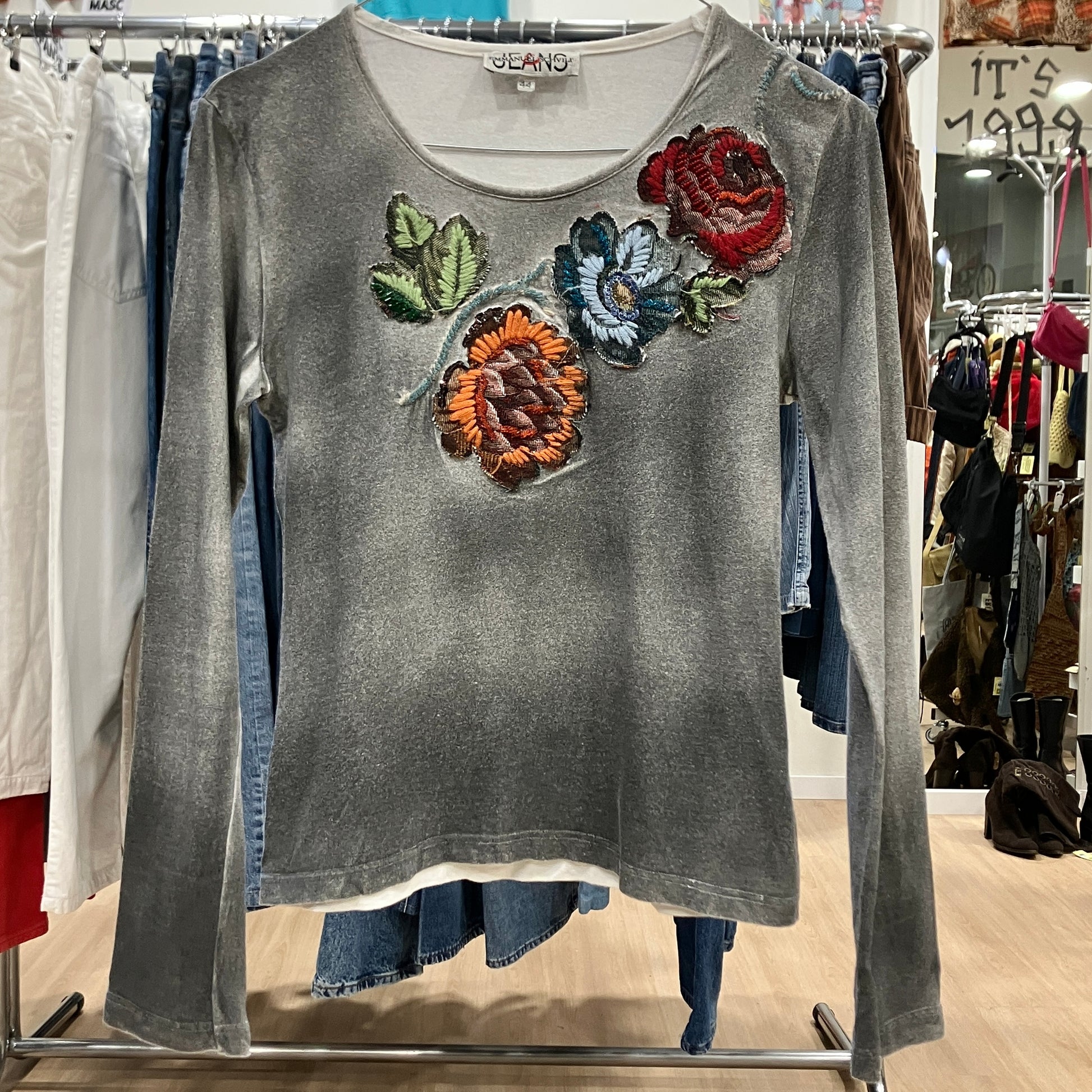 Gray long-sleeve shirt with colorful floral appliqués on a clothing rack