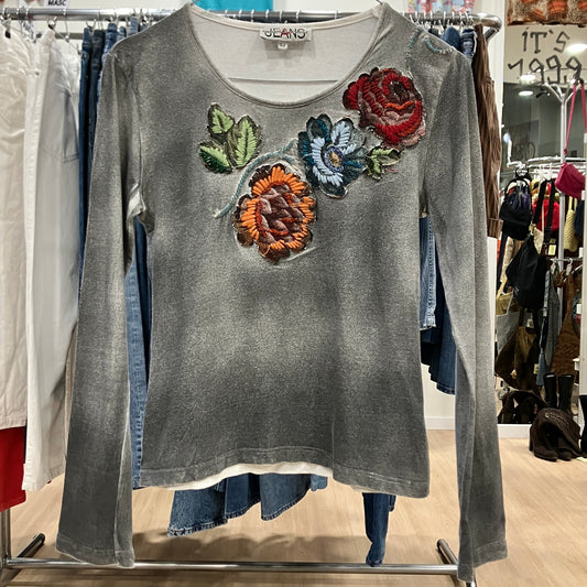 Gray long-sleeve shirt with colorful floral appliqués on a clothing rack