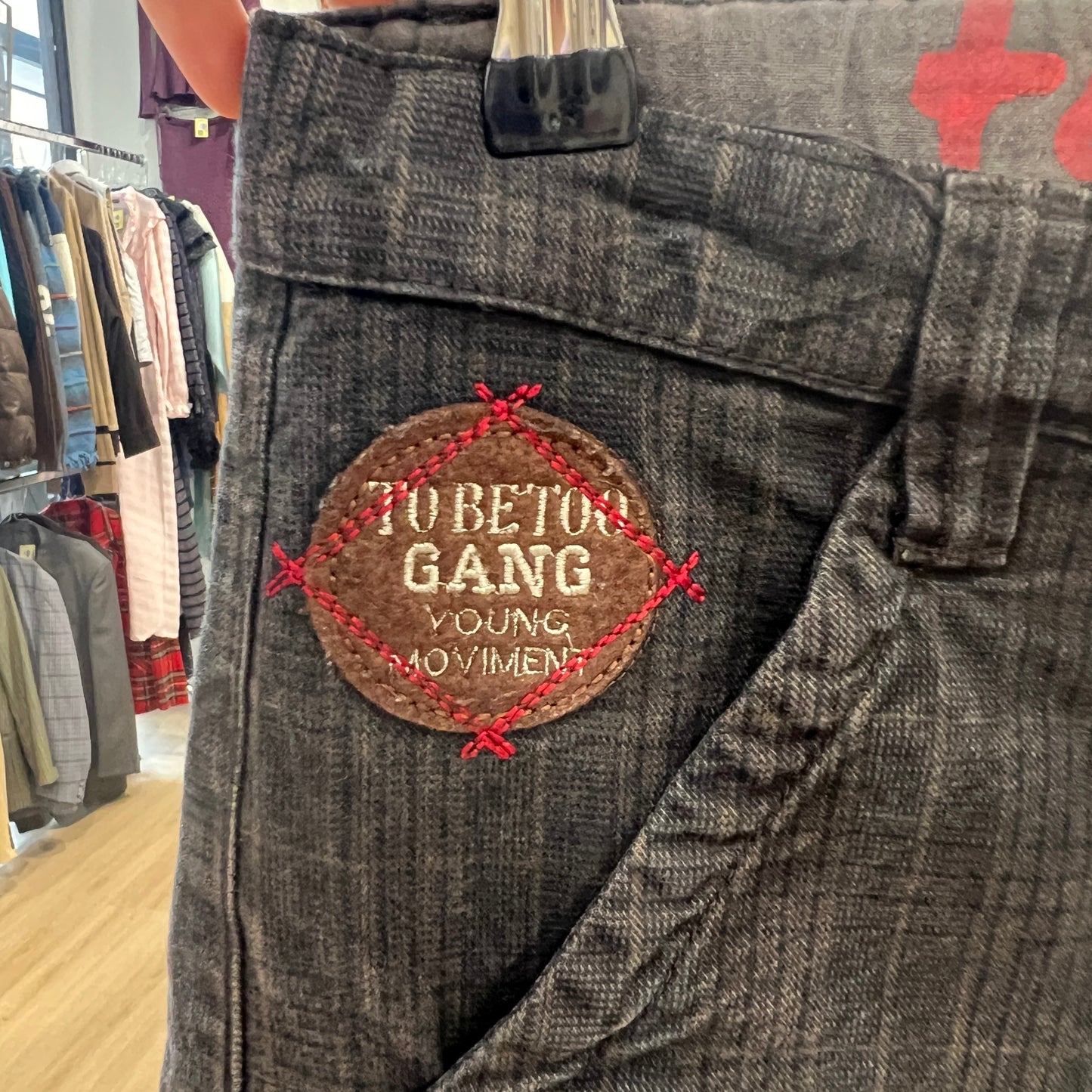 Gray plaid pants with a patch labeled 'To Be Too Gang Young Movement' in a clothing store