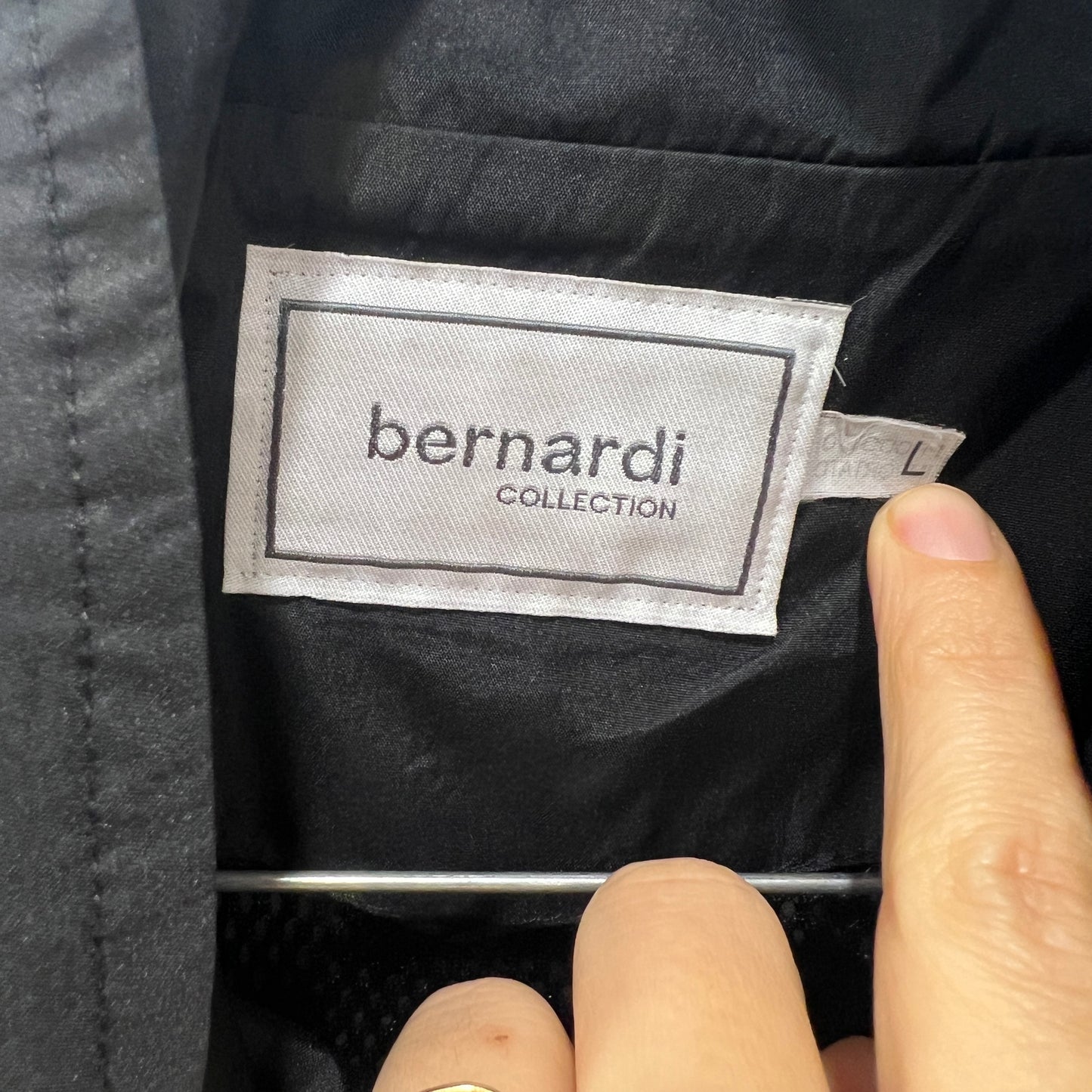 Close-up of a 'bernardi collection' label on a black garment with a finger pointing at it