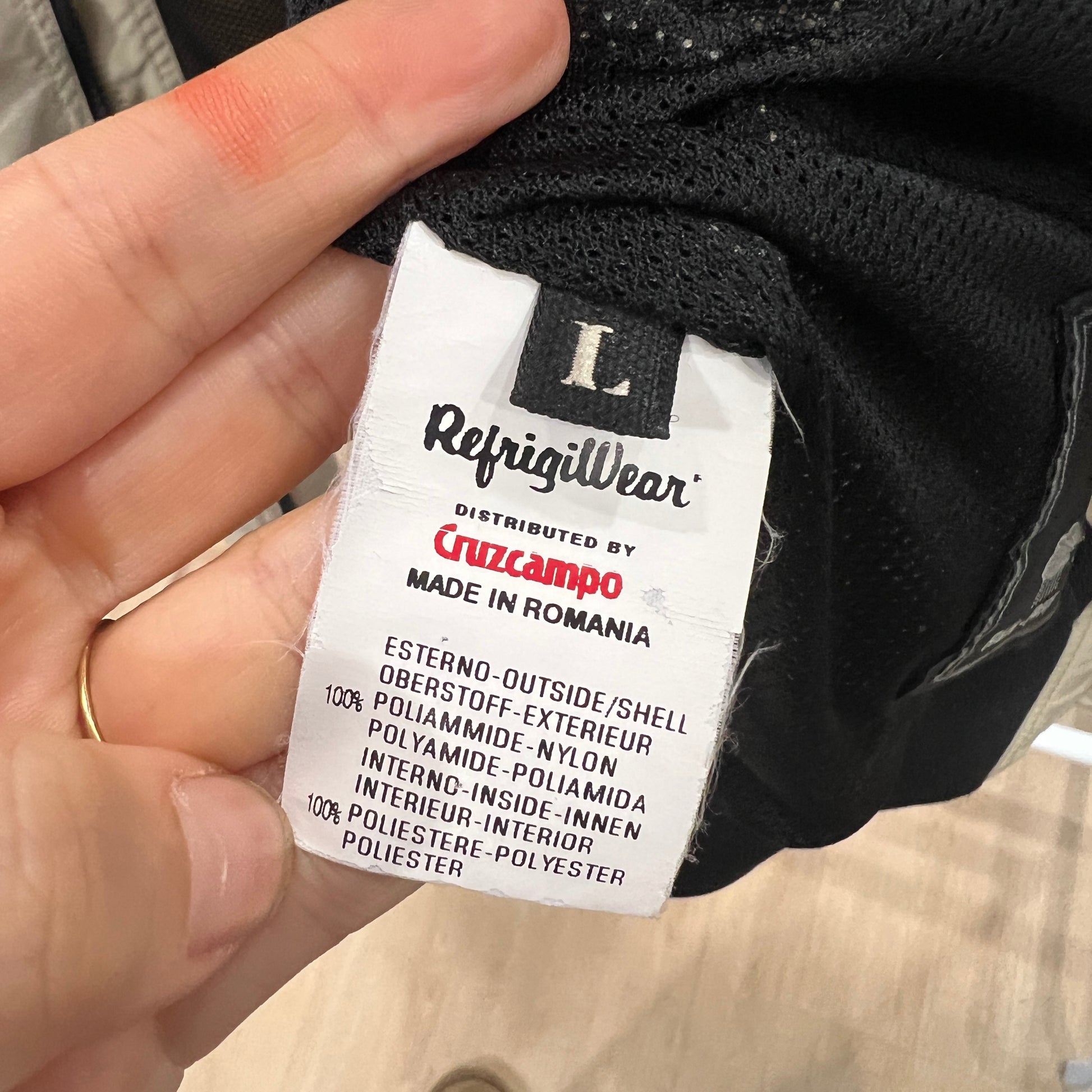 Clothing label with 'RefrigilWear' and 'Cruzcampo' branding, held by a hand