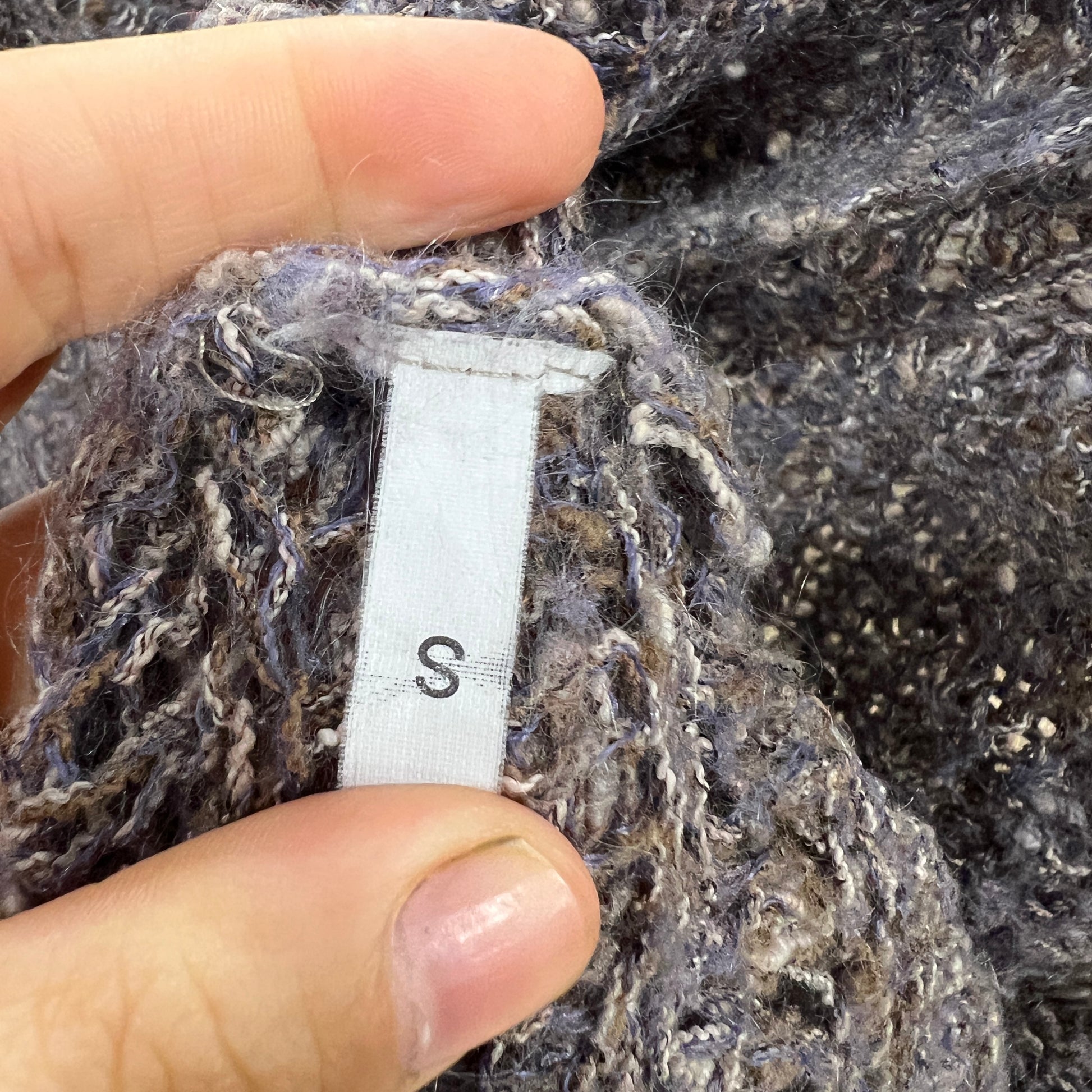 Close-up of a textured fabric with a size label 'S' held by a hand