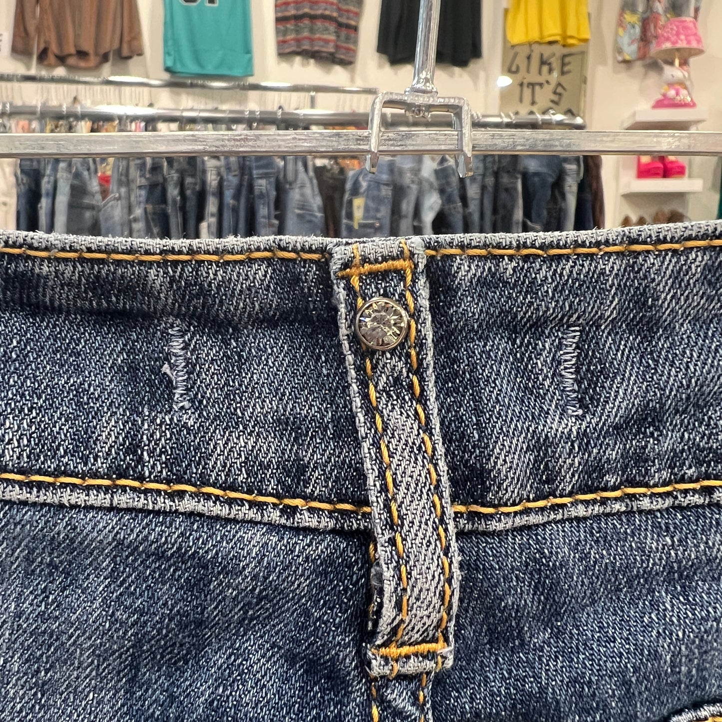 Close-up of blue jeans with a button and yellow stitching in a store setting