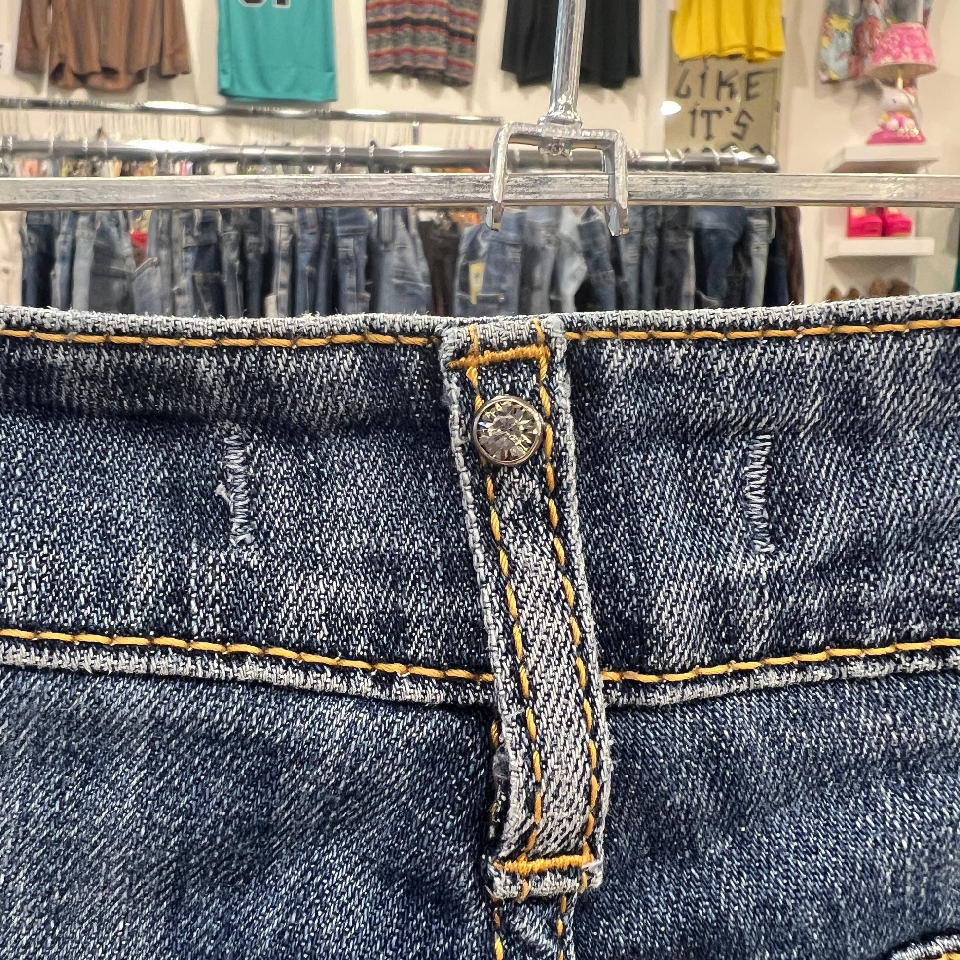 Close-up of blue jeans with a button and yellow stitching in a store setting