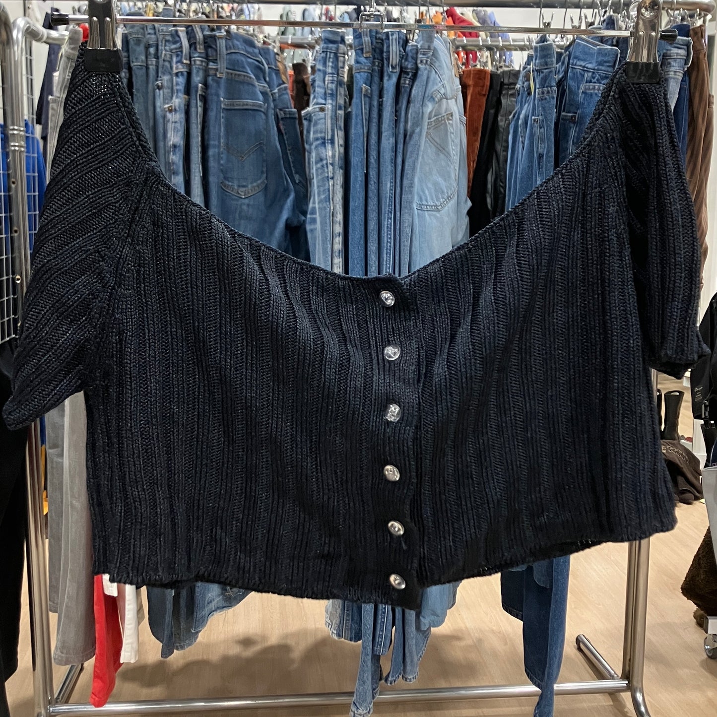 Black button-up top on a rack with jeans in a store setting
