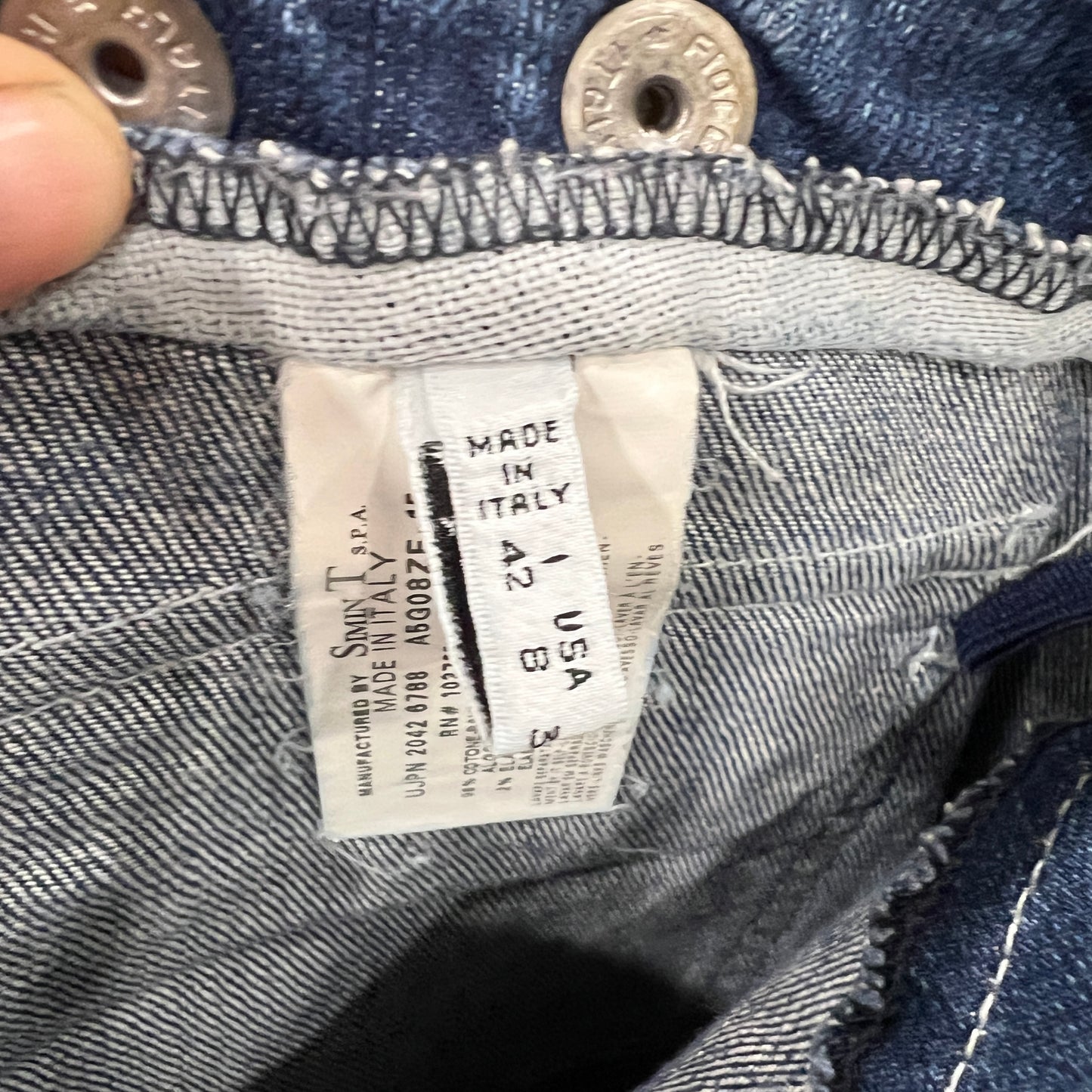 Close-up of the inner size and manufacturing label on a pair of Armani Jeans denim pants, showing “Made in Italy” and size info alongside visible stitching and metal buttons
