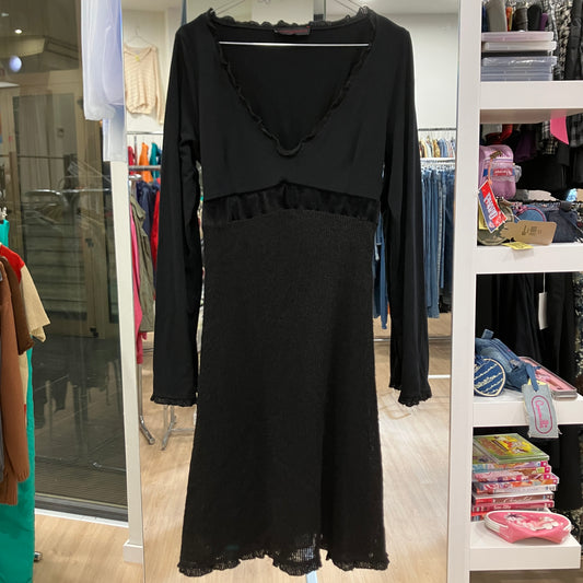 Black dress on a hanger in a store setting with shelves and clothing in the background