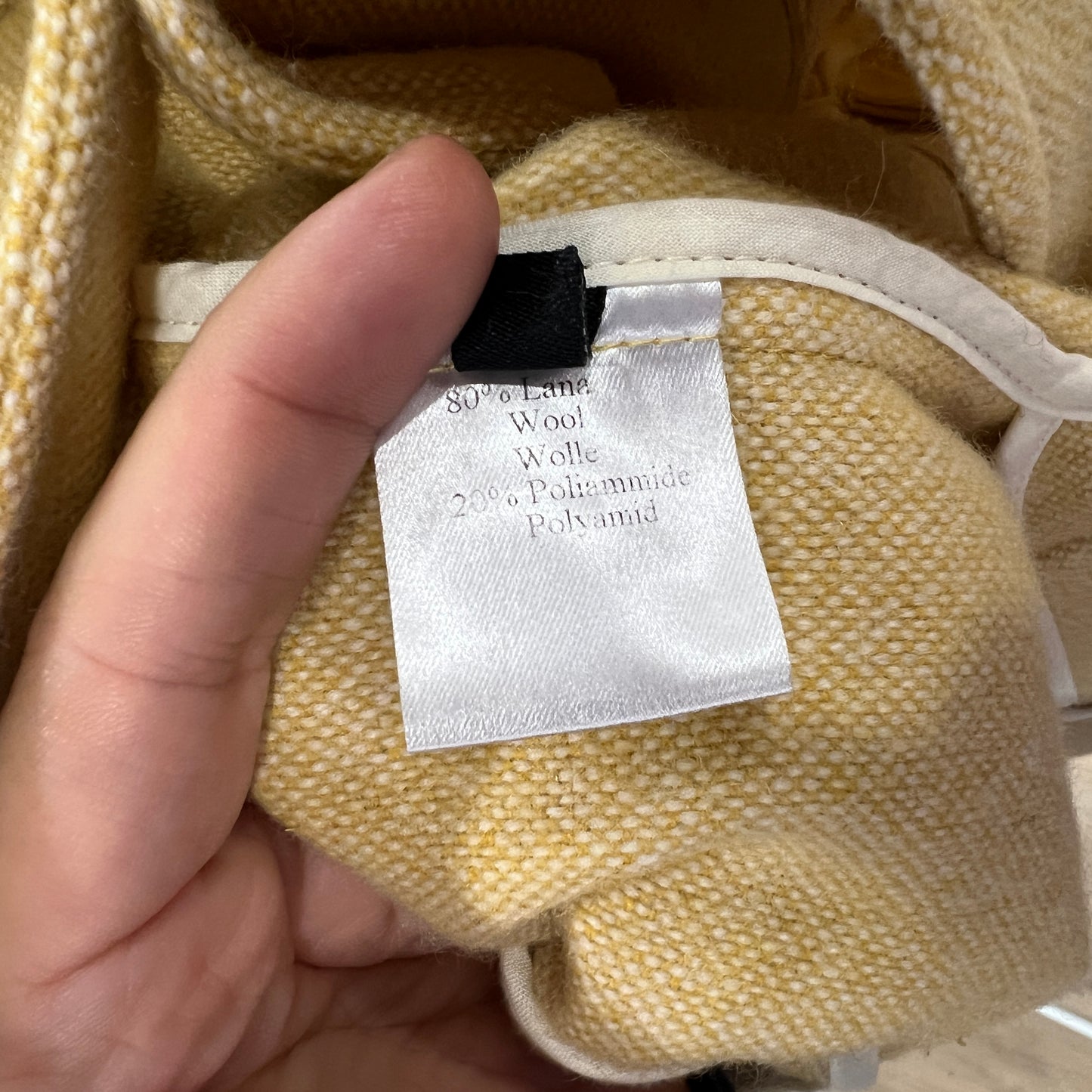 Hand holding a fabric tag on a yellow textured fabric