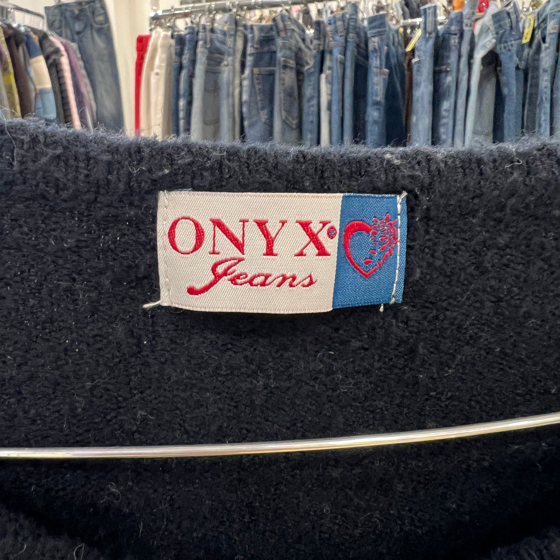 Black jacket with 'ONYX Jeans' label against a background of jeans on hangers