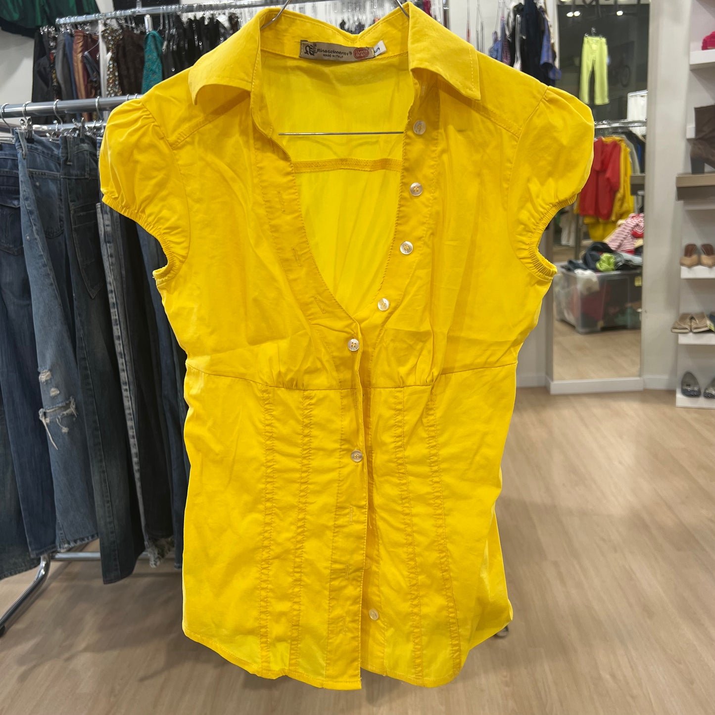 Yellow sleeveless button-up shirt on a hanger in a store setting