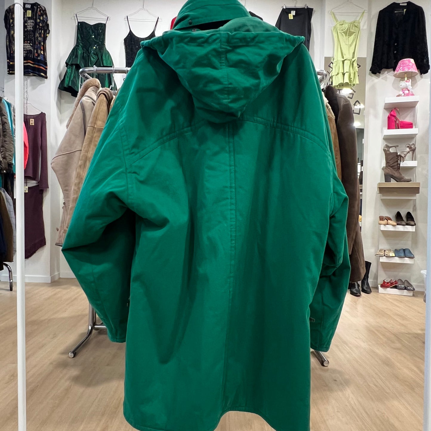 Green raincoat in a clothing store with racks of clothes and shoes in the background