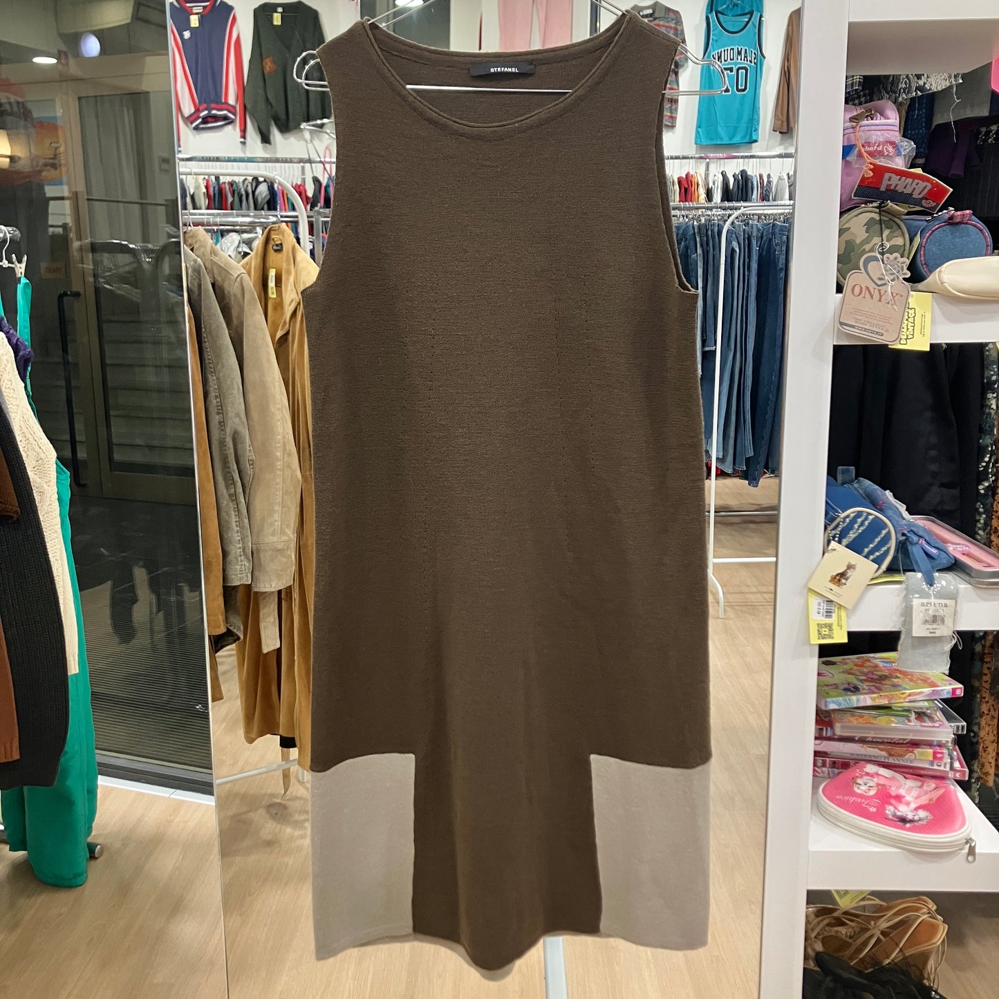 Brown sleeveless dress hanging in a store with clothing racks and shelves in the background