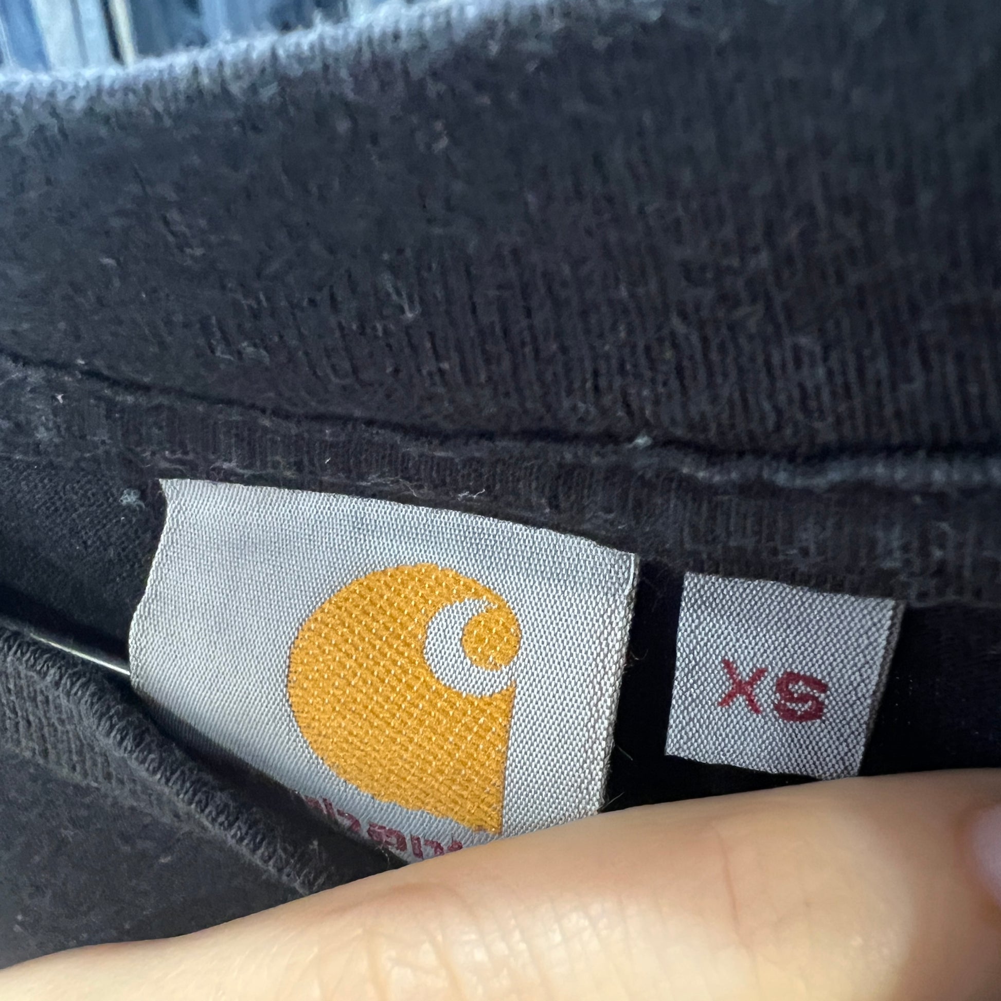 Close-up of a Carhartt label on a piece of clothing with a finger pointing to it