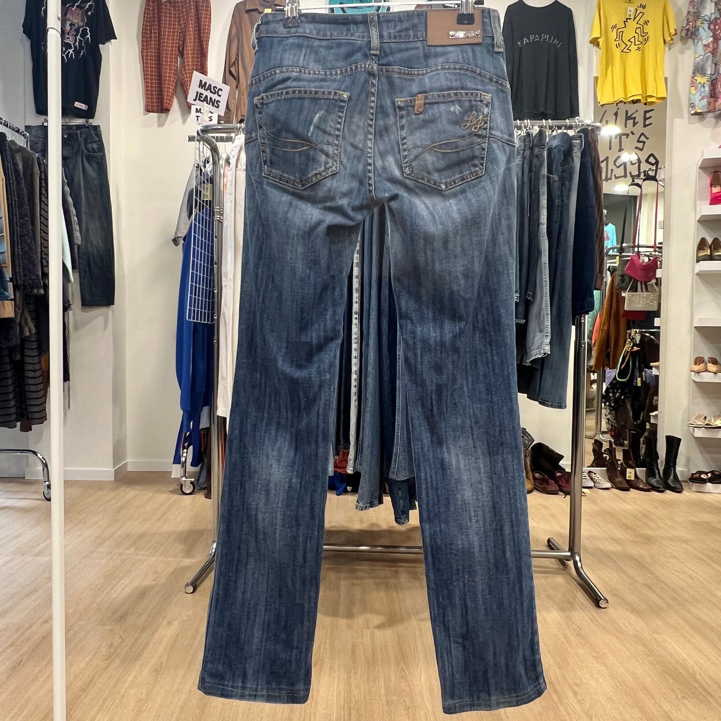 Blue jeans displayed on a rack in a store setting with various clothing items in the background