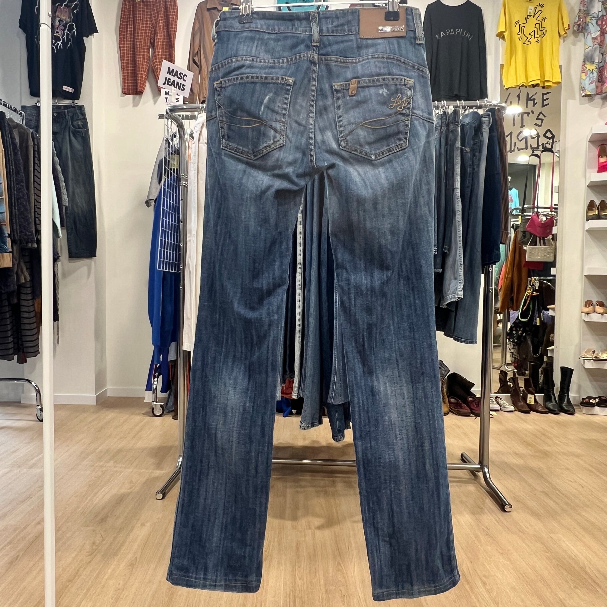 Blue jeans displayed on a rack in a store setting with various clothing items in the background