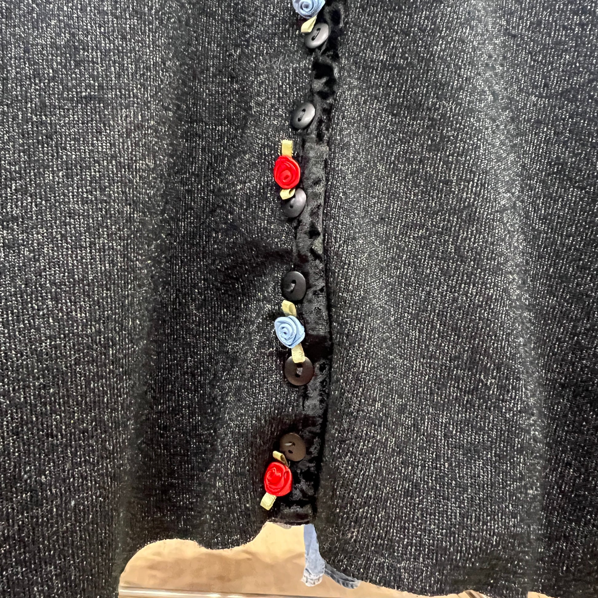 Black dress with colorful buttons on a hanger against a dark background