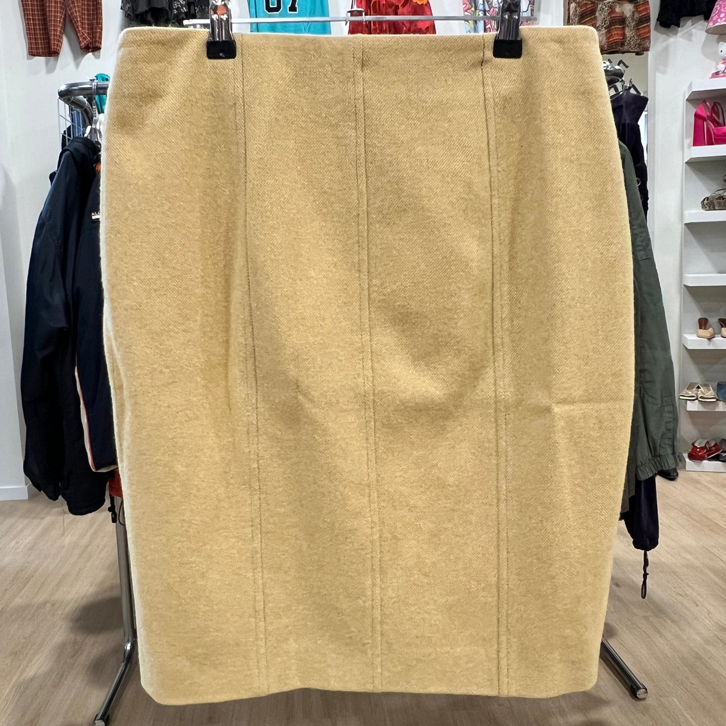 Front view of a beige wool pencil skirt with clean vertical seam detailing, displayed on a hanger inside a vintage clothing

