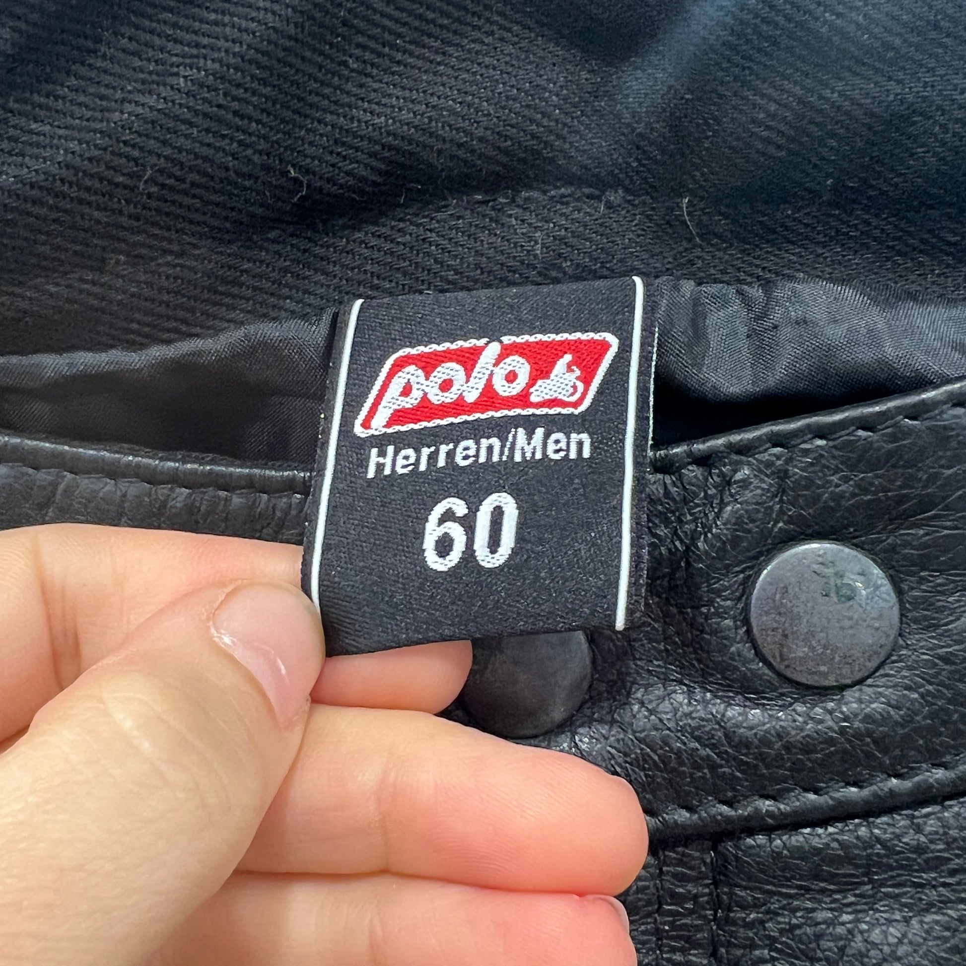 Close-up of a label on a black leather pants with a hand holding it
