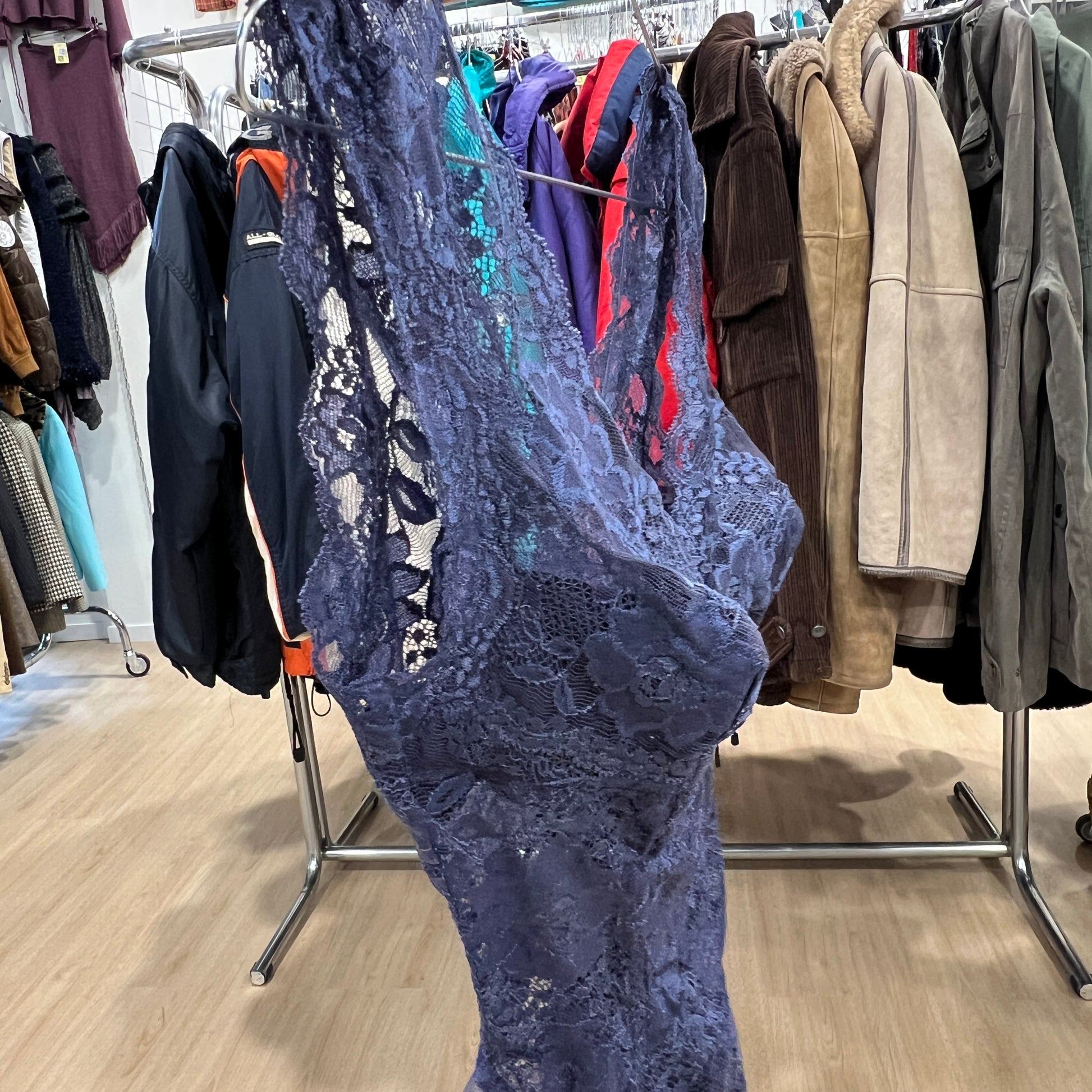 Blue lace dress hanging on a rack with other clothing in a store setting