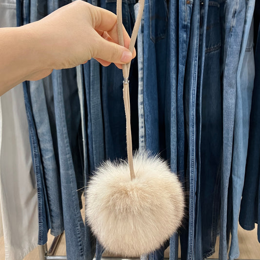 Fuzzy white keychain held in front of hanging jeans