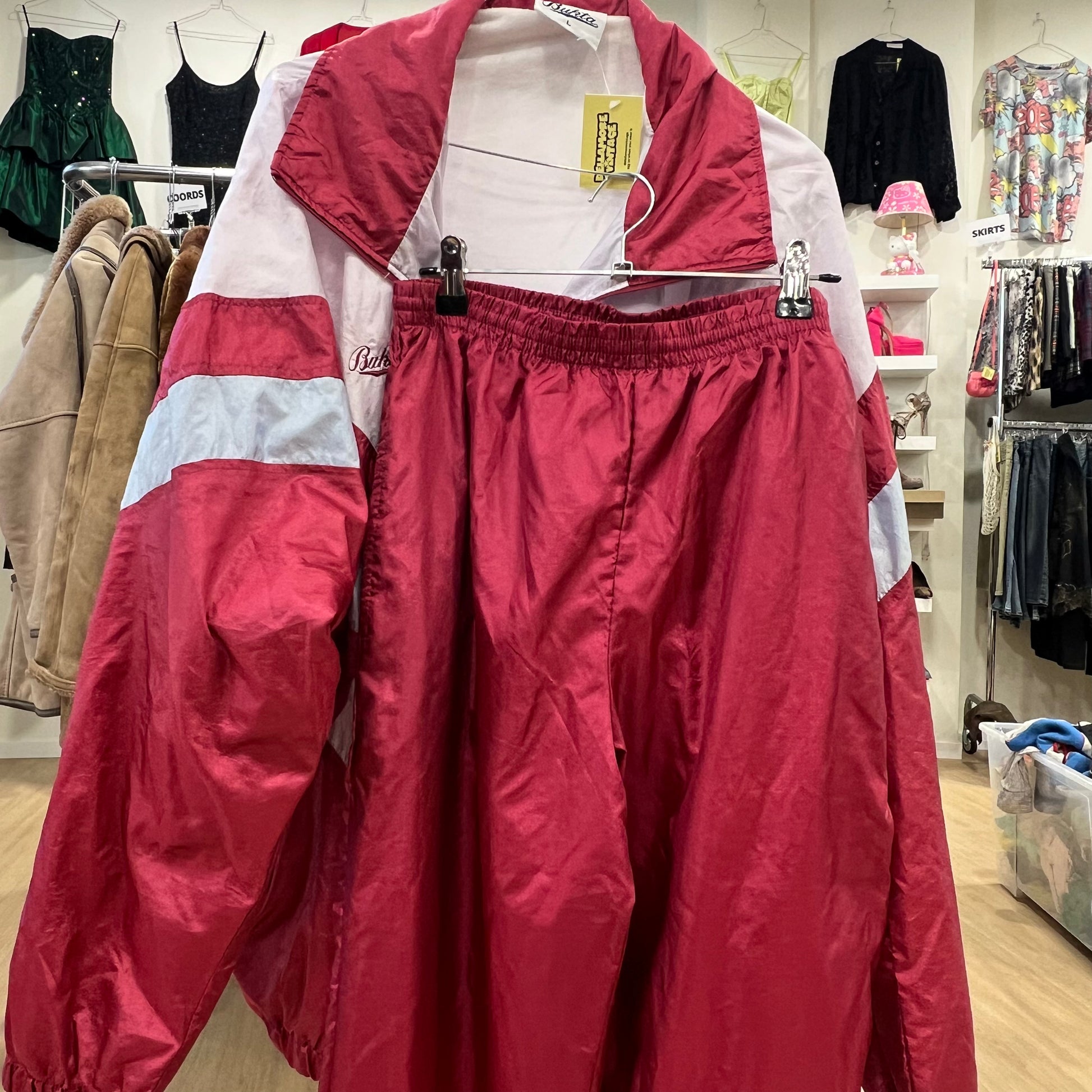 Vintage red and white tracksuit with elastic waist pants and color block jacket hanging on a rack in a retro clothing store