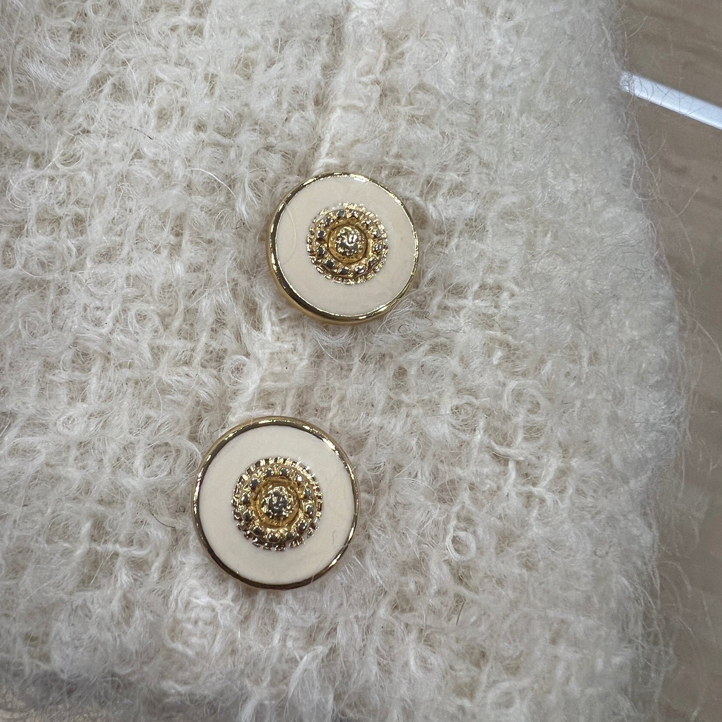 Pair of round buttons with gold accents on a textured white fabric background