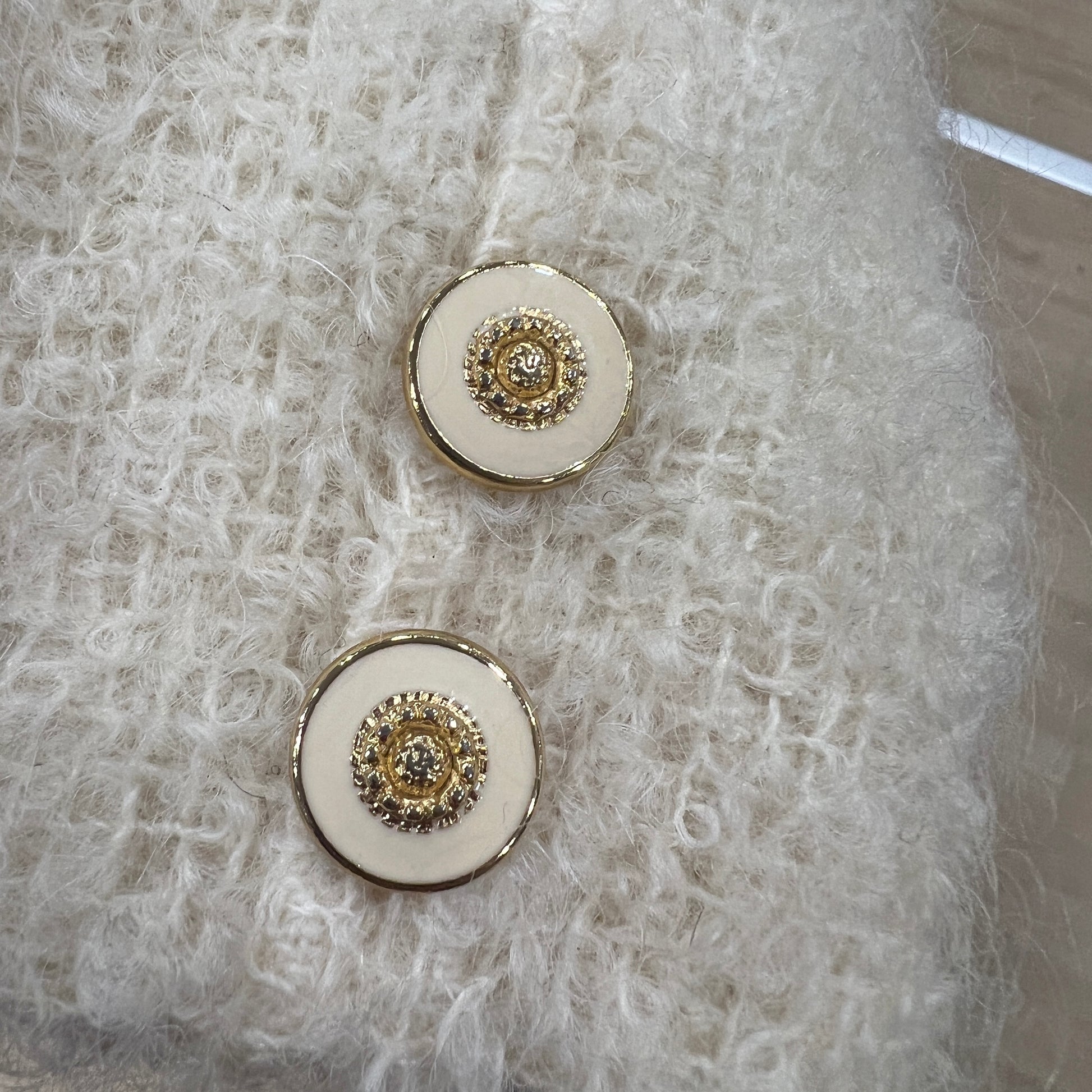 Pair of round buttons with gold accents on a textured white fabric background