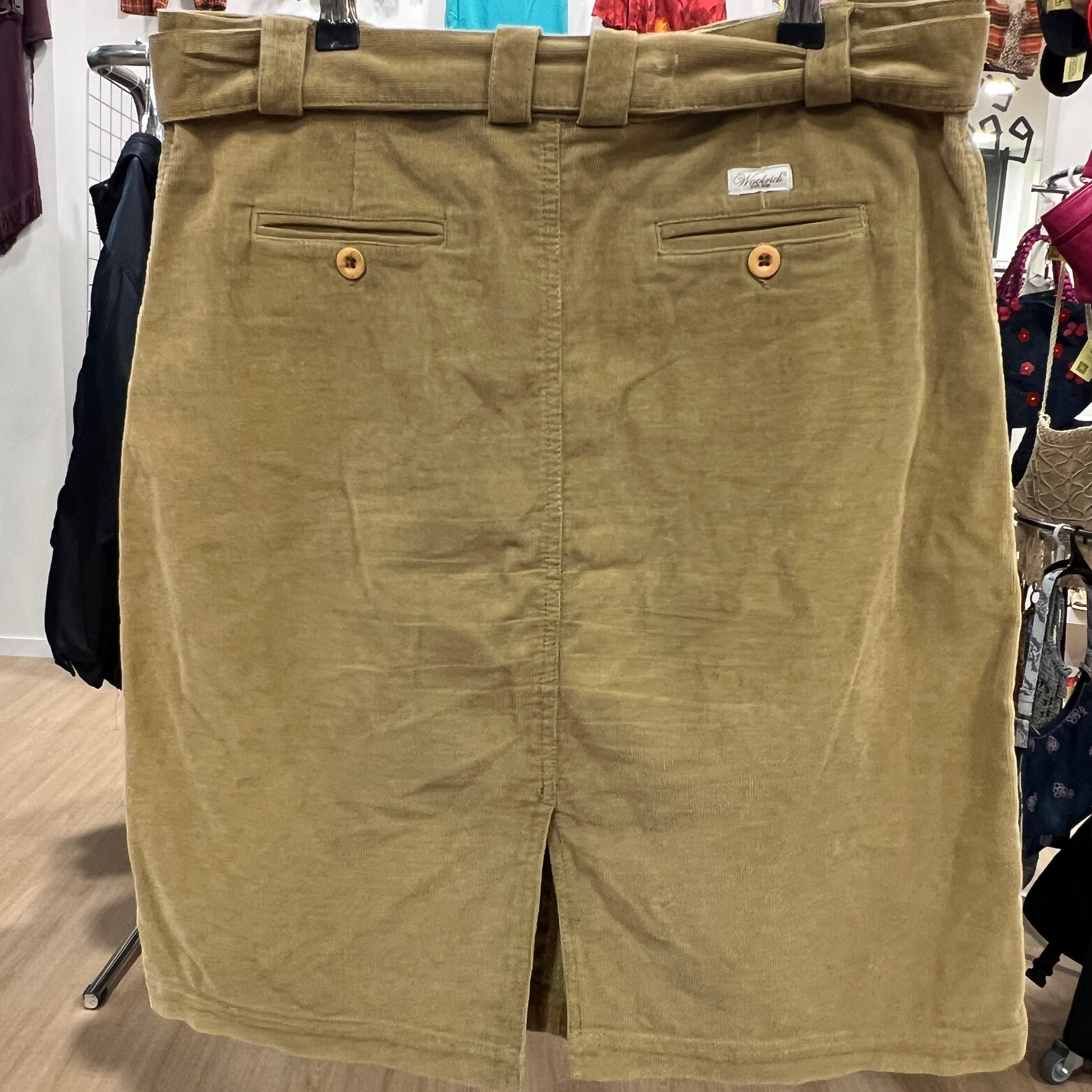 Camel skirt with a belt and button details on a hanger against a store background