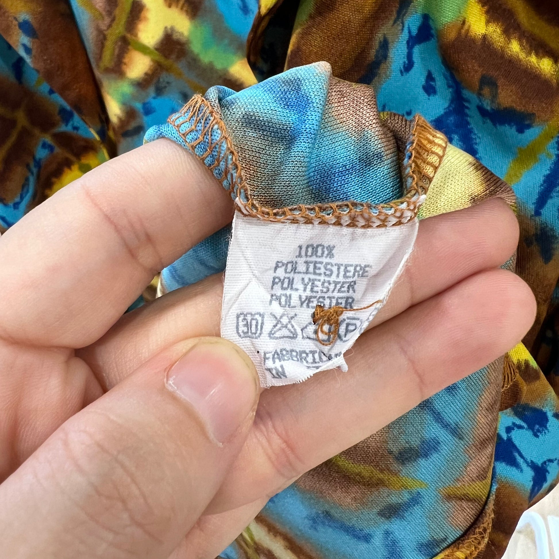 Hand holding a fabric tag with clothing information against a colorful background