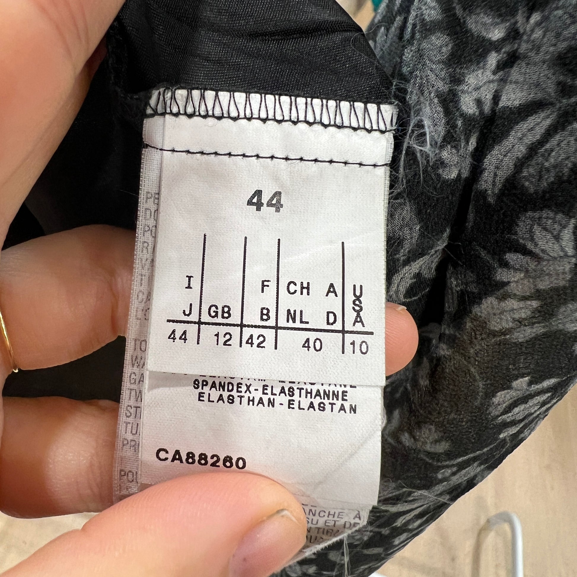 Close-up of a size conversion label inside a black floral skirt, showing EU size 44 alongside UK, FR, NL, DE, and US equivalents, with elastane composition noted below
