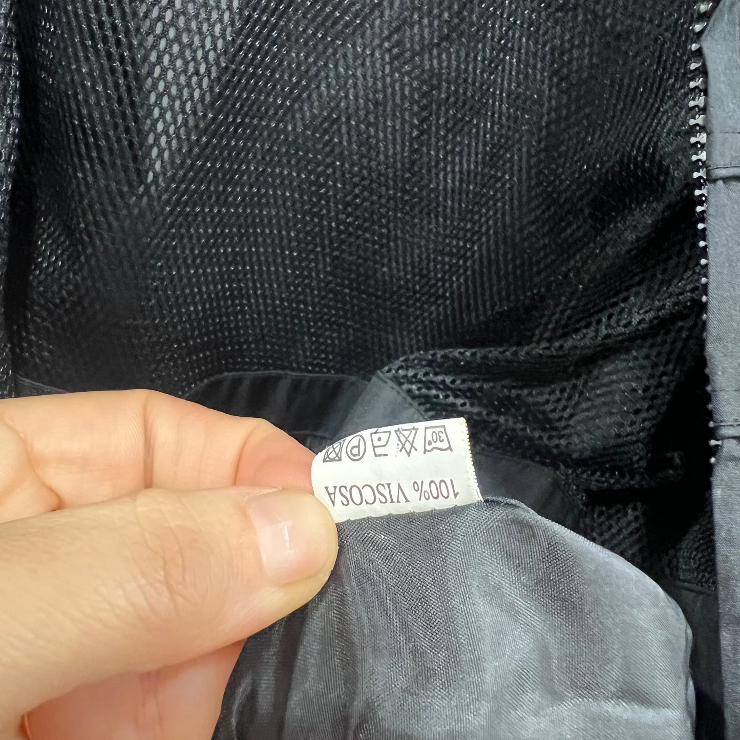 Hand holding a label on a black fabric garment with visible text