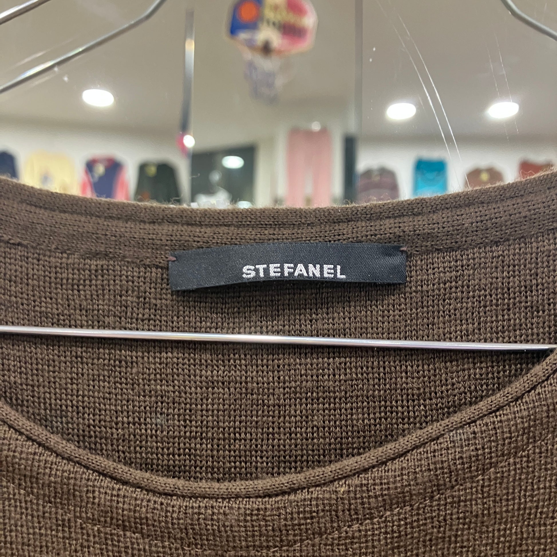 Brown fabric with a 'STEFANEL' label on a hanger in a store setting
