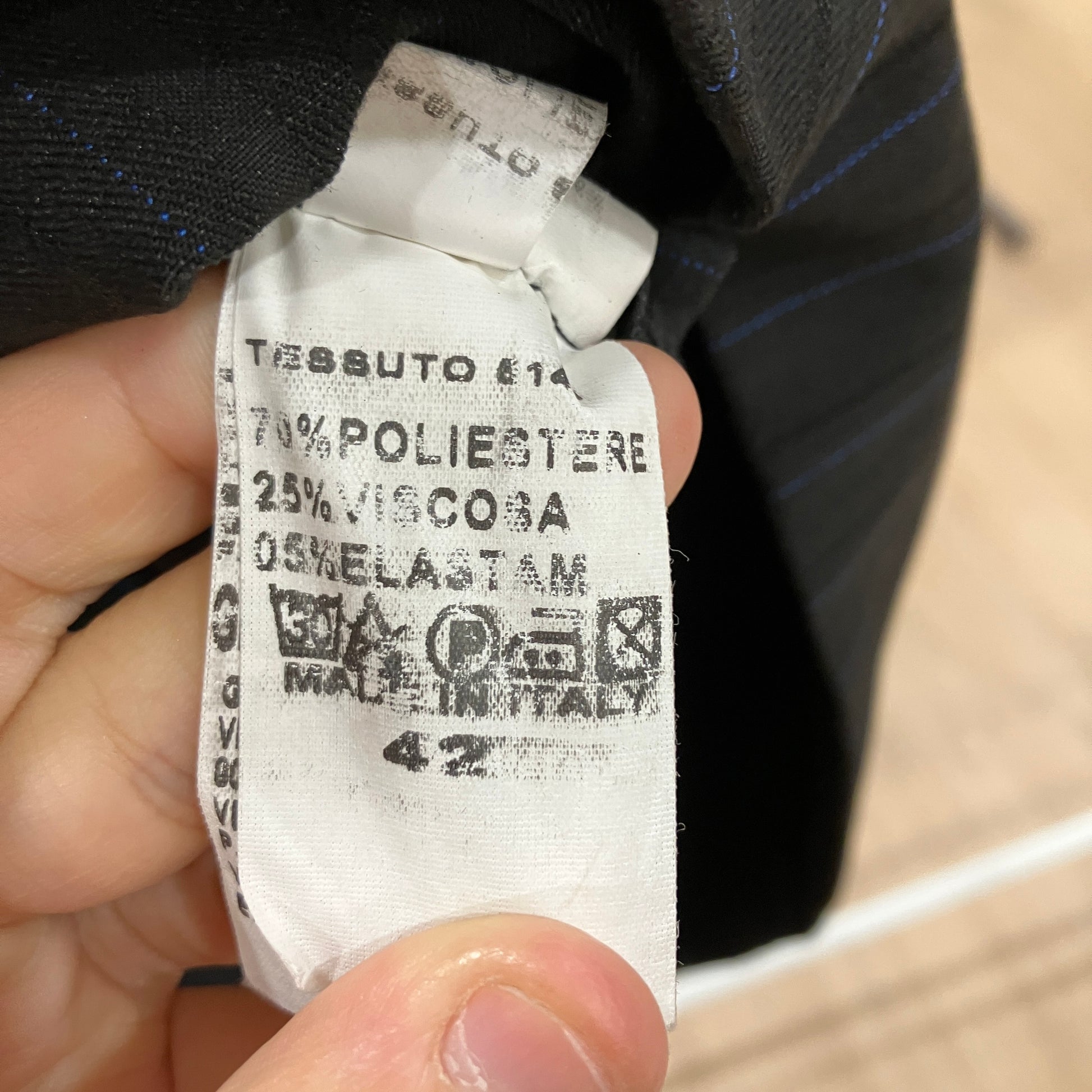 Close-up of a fabric label held by a hand, showing text and symbols