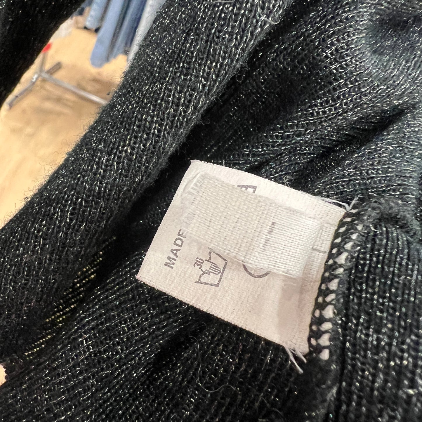 Close-up of a partially folded inner care label inside a black knit garment, showing washing symbols and the word ‘MADE’ while the tag rests between the textured fabric
