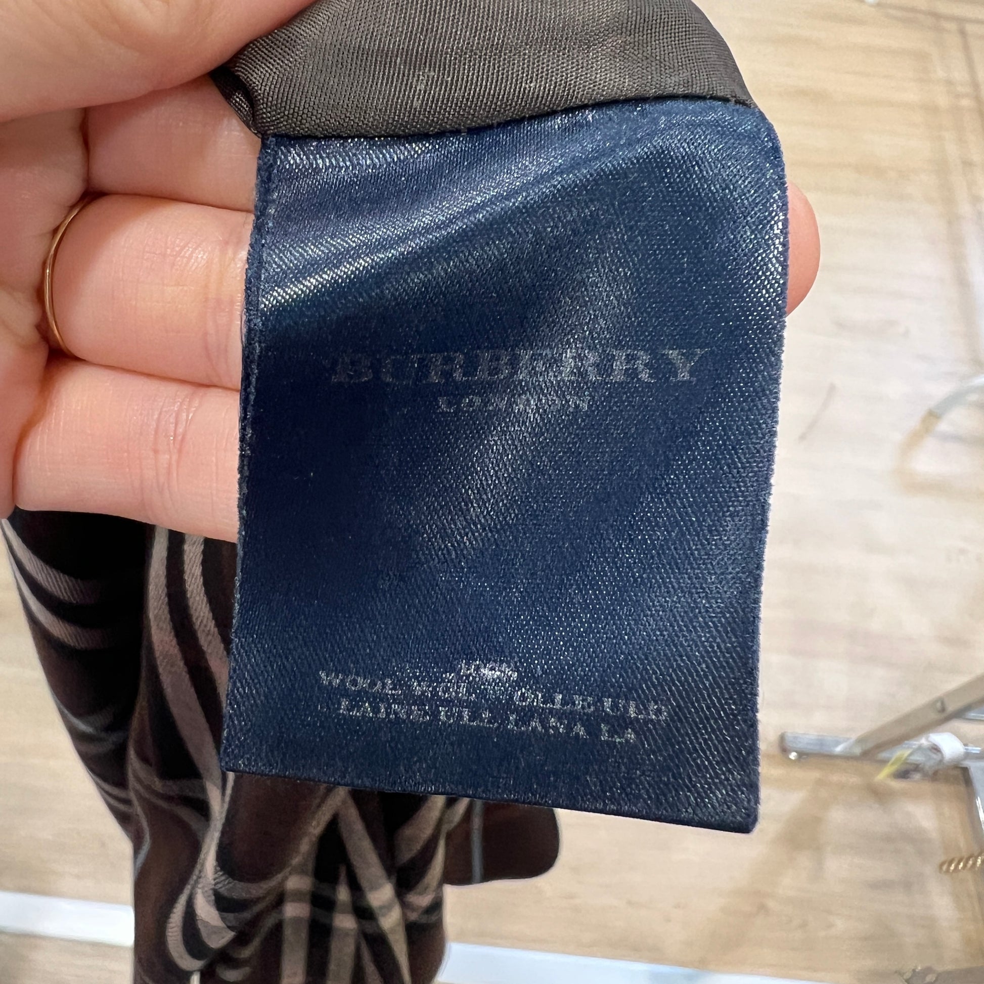 Close-up of a dark blue Burberry London label on a striped skirt, showing worn silver lettering and fabric details while the tag is held between two fingers
