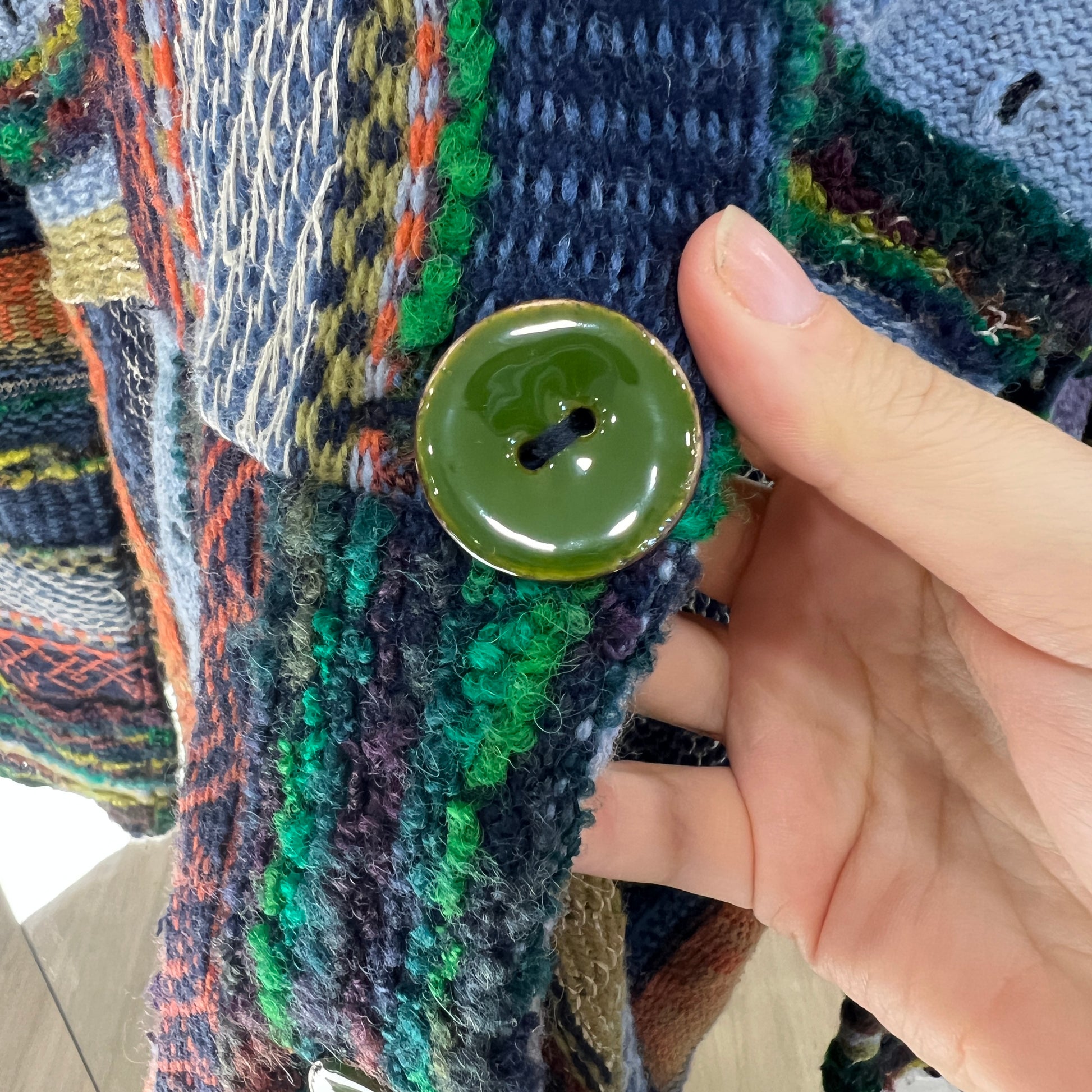 Hand holding a green button on a textured fabric background