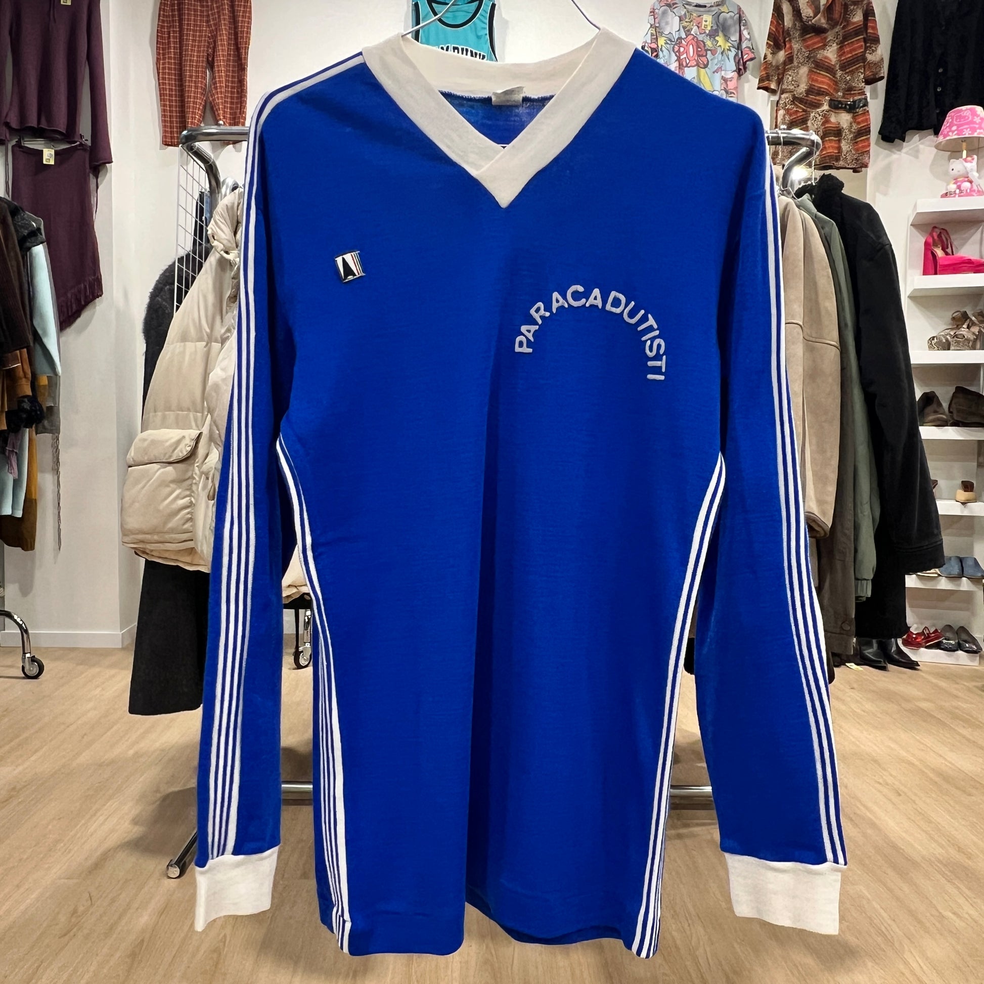 Blue long-sleeve shirt with 'Paracadutisti' branding in a clothing store setting
