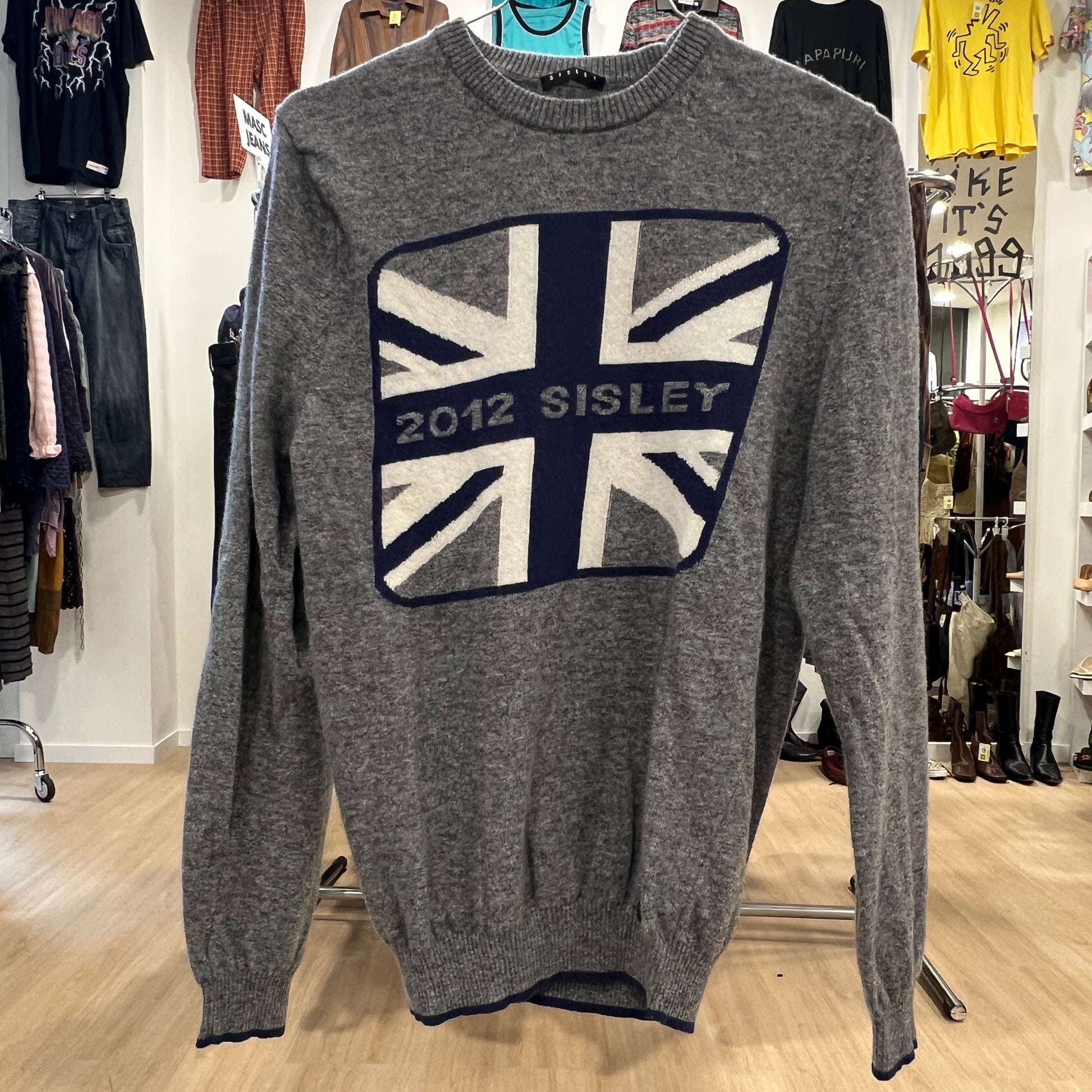 Gray sweater with Union Jack design and '2012 SISLEY' text in a clothing store setting