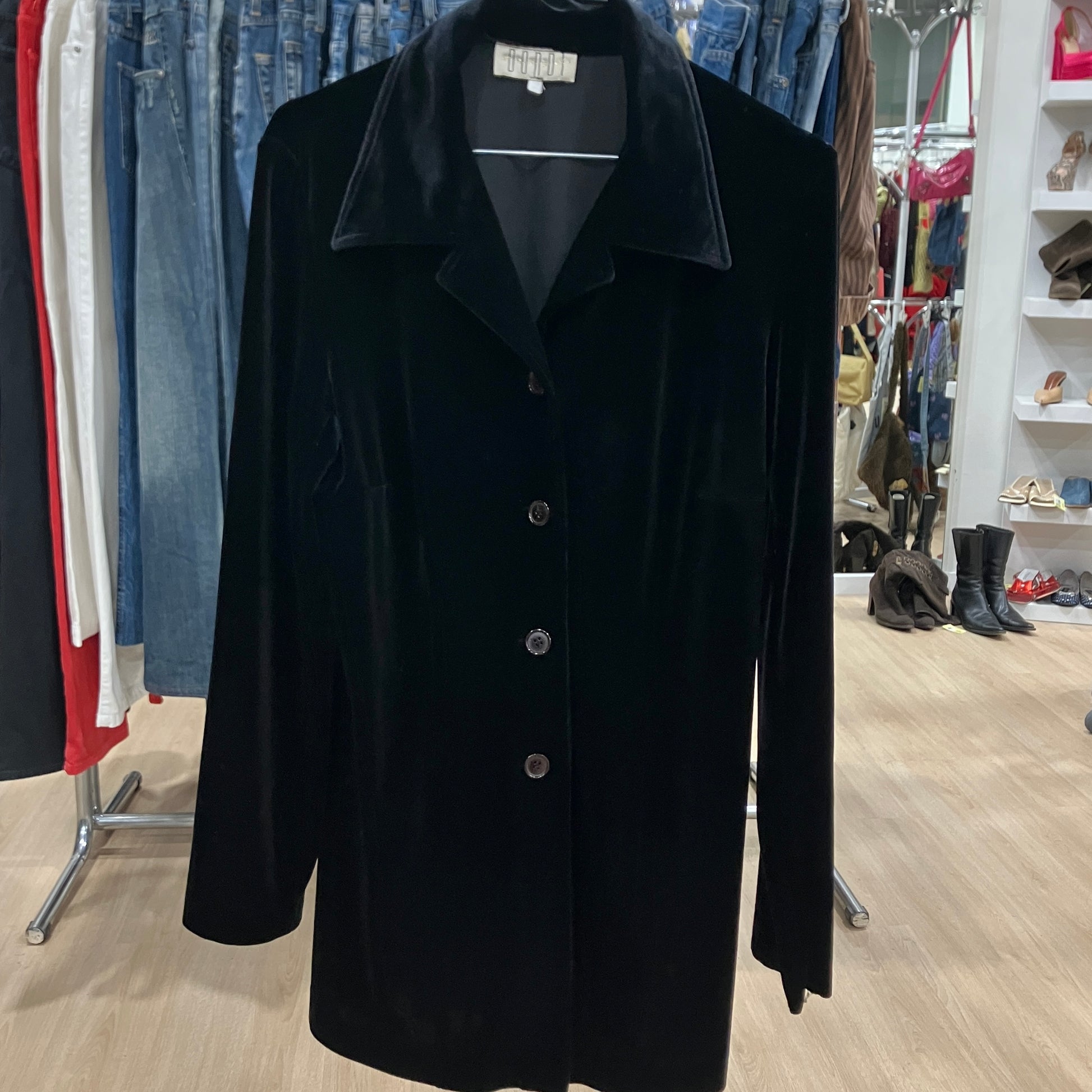 Black coat on a hanger in a clothing store with jeans and shoes in the background