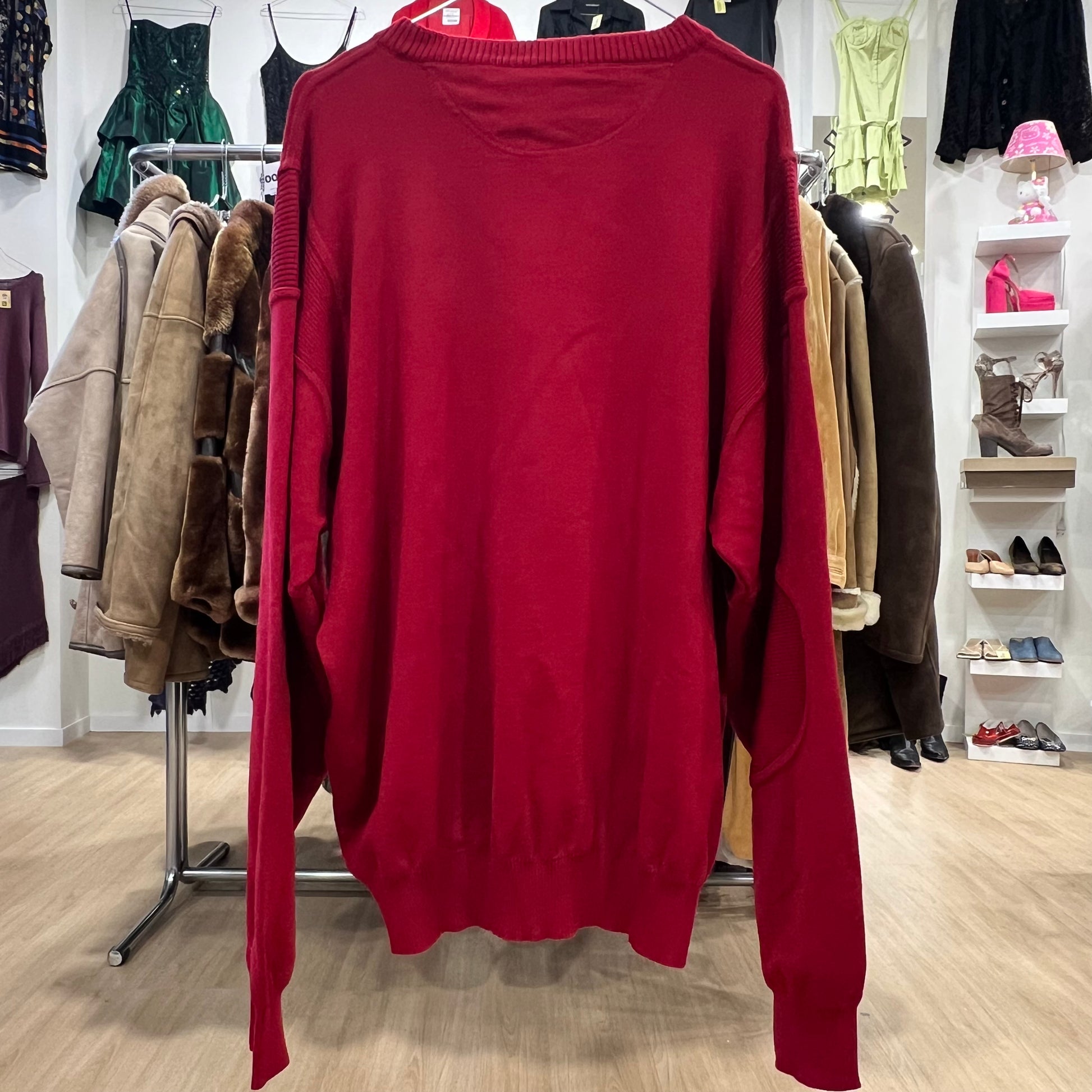 Red sweater hanging in a clothing store with various garments in the background
