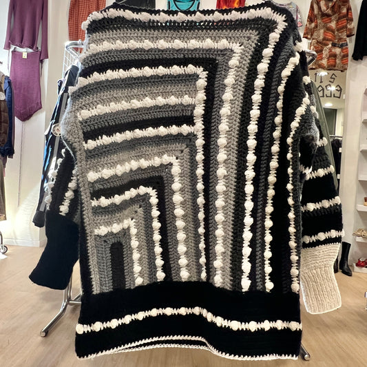 Black and gray striped blanket with white pom-poms in a store setting